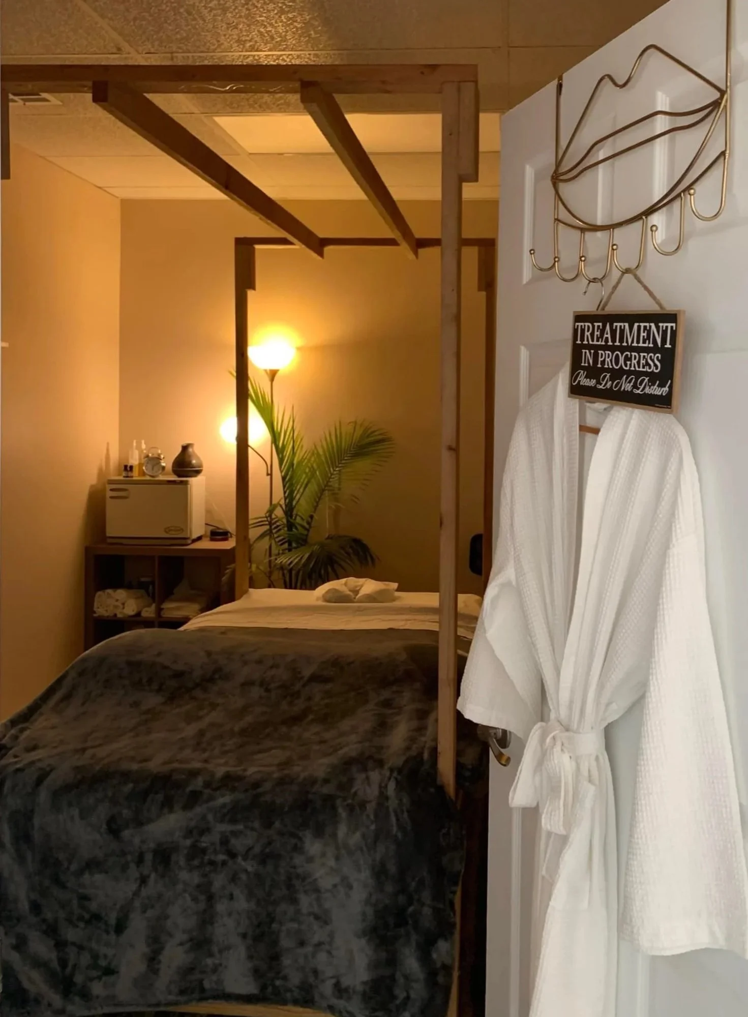 Massage room bed with tall plant and white robe hanging on door