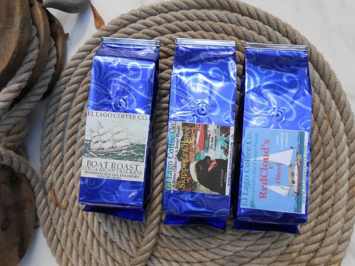 Three blue foil bags of coffee with sailing themes on backdrop of coiled rope