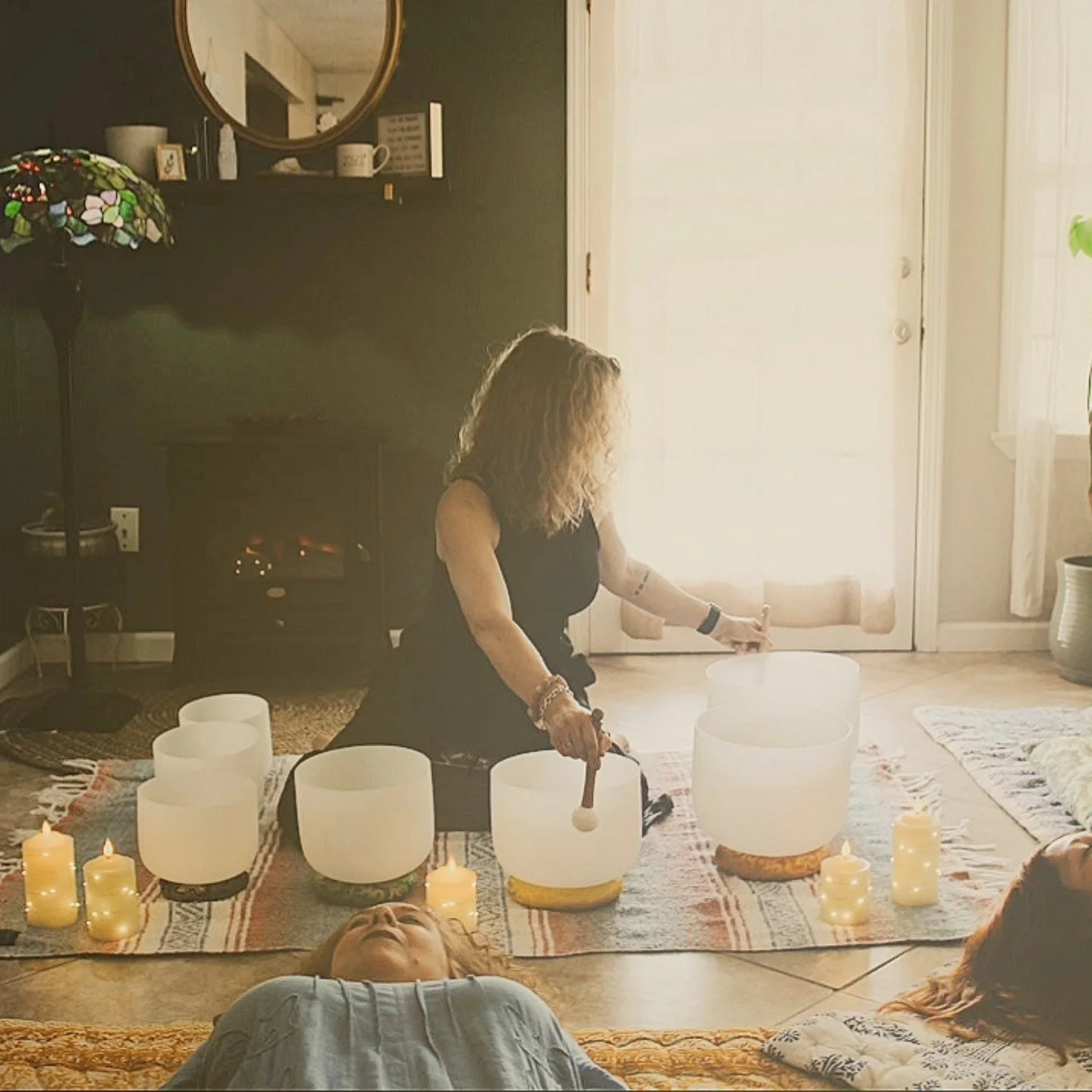 Woman sitting on floor in dim room with white bowls for sound bath