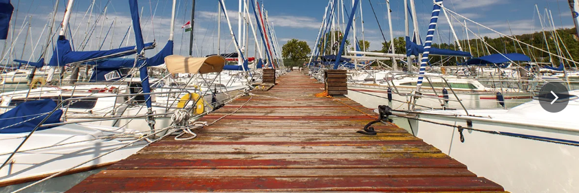 Sailboats with blue sails and ropes tied to posts on a wooden walkway