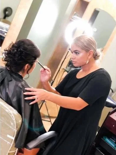 Stylist providing make-up service to woman in salon chair and cape