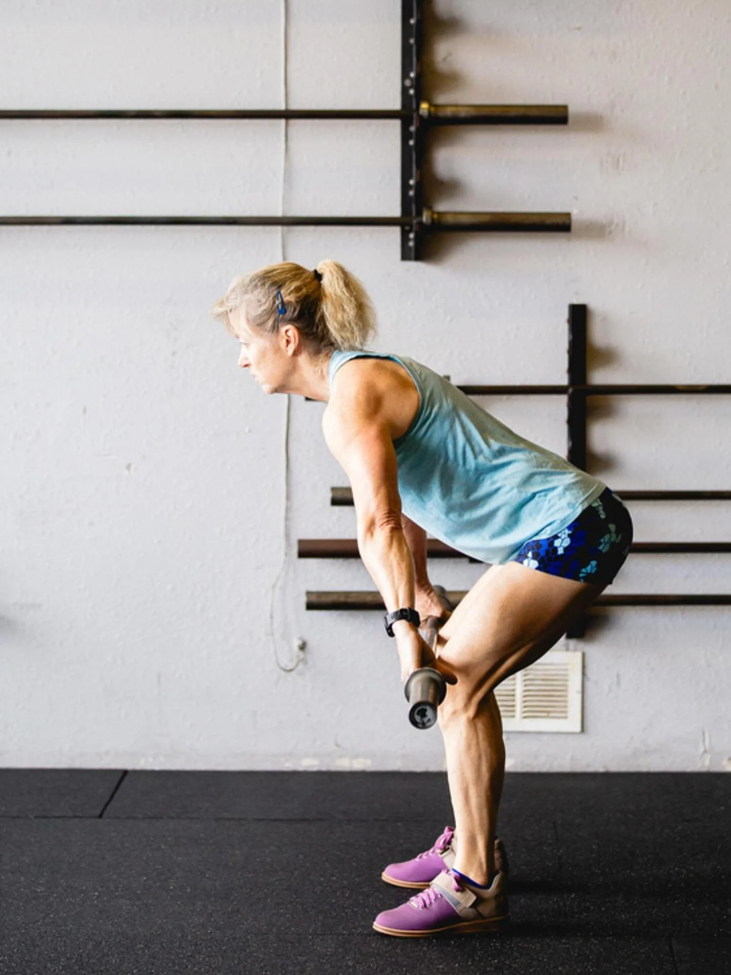 Woman wearing a blue top and shorts lifting weight bar in a gym