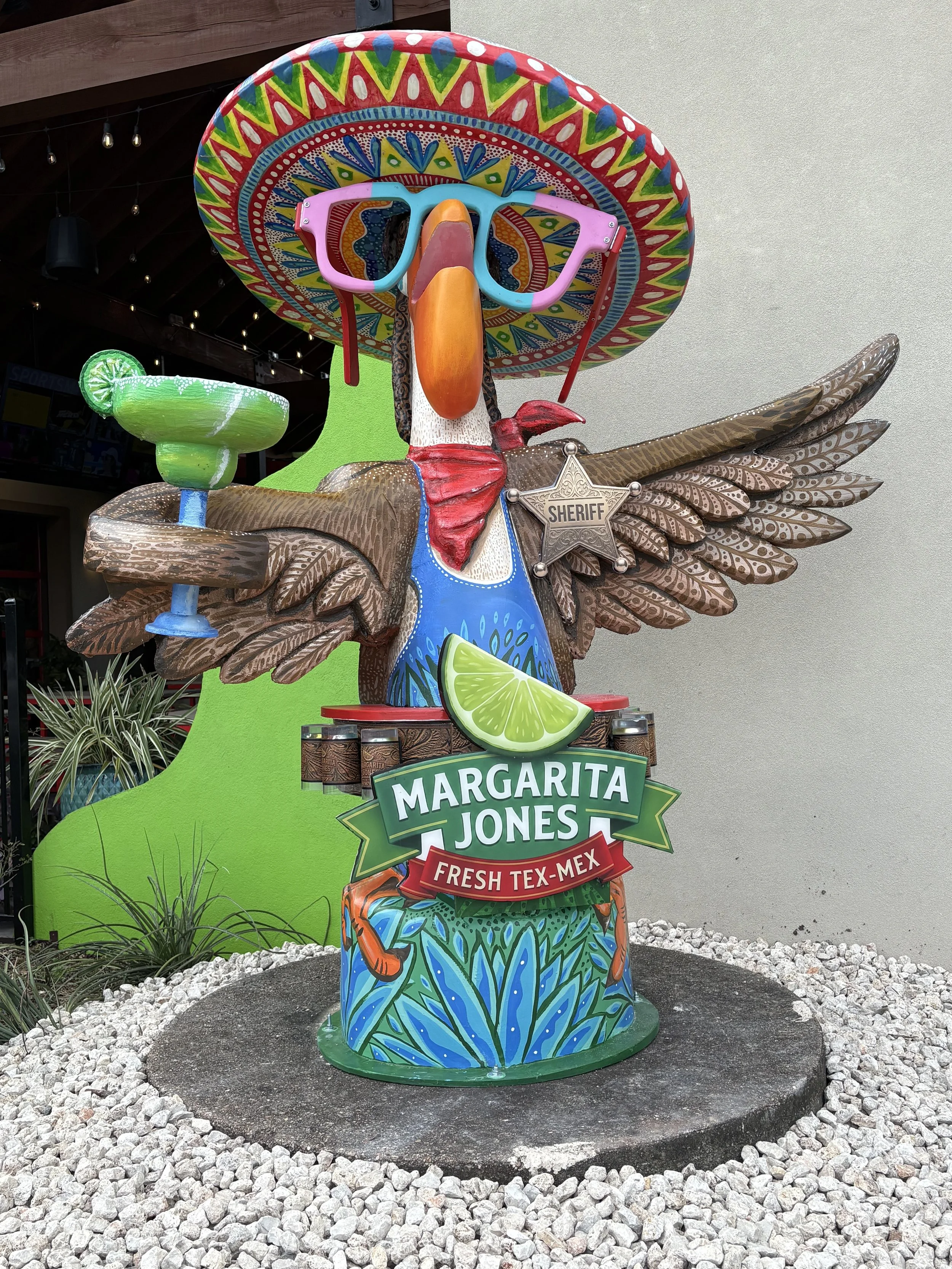 A colorful painting pelican structure wearing a sombrero and sheriff badge, holding a margarita glass, with the words Margarita Jones Fresh Tex Mex