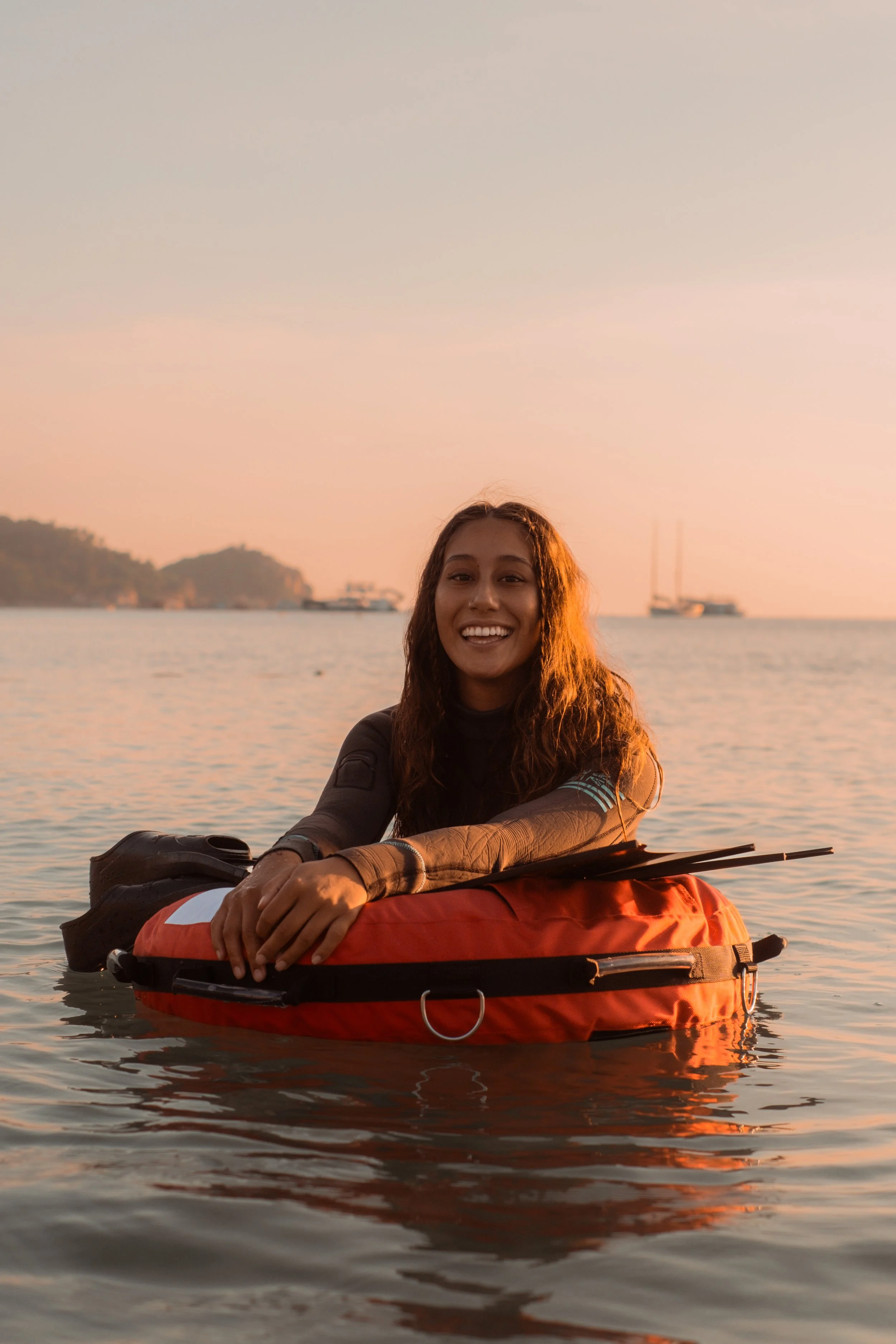 Person smiling while sitting on a flotation device in a calm sea during sunset.