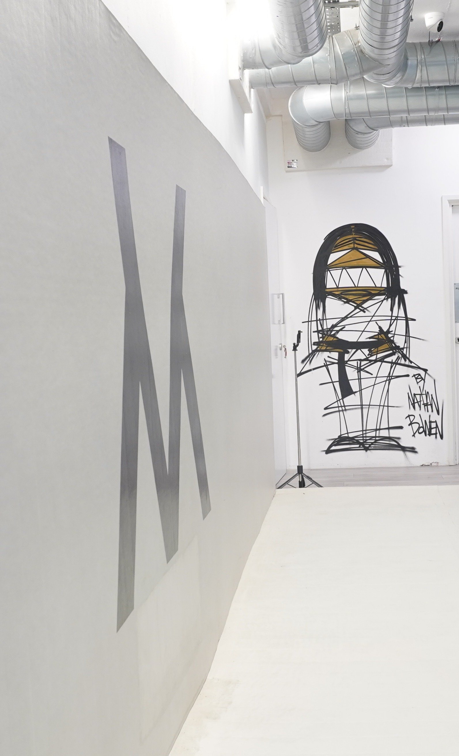 Gallery space with white walls, metallic ventilation pipes on the ceiling, and a wire sculpture of a futuristic head with the words 'Nathan Bowen' at the bottom right.