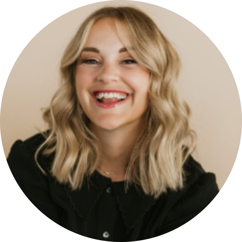 A young woman with wavy blonde hair smiling and sticking out her tongue, wearing a black top, against a light background with a yellow border.
