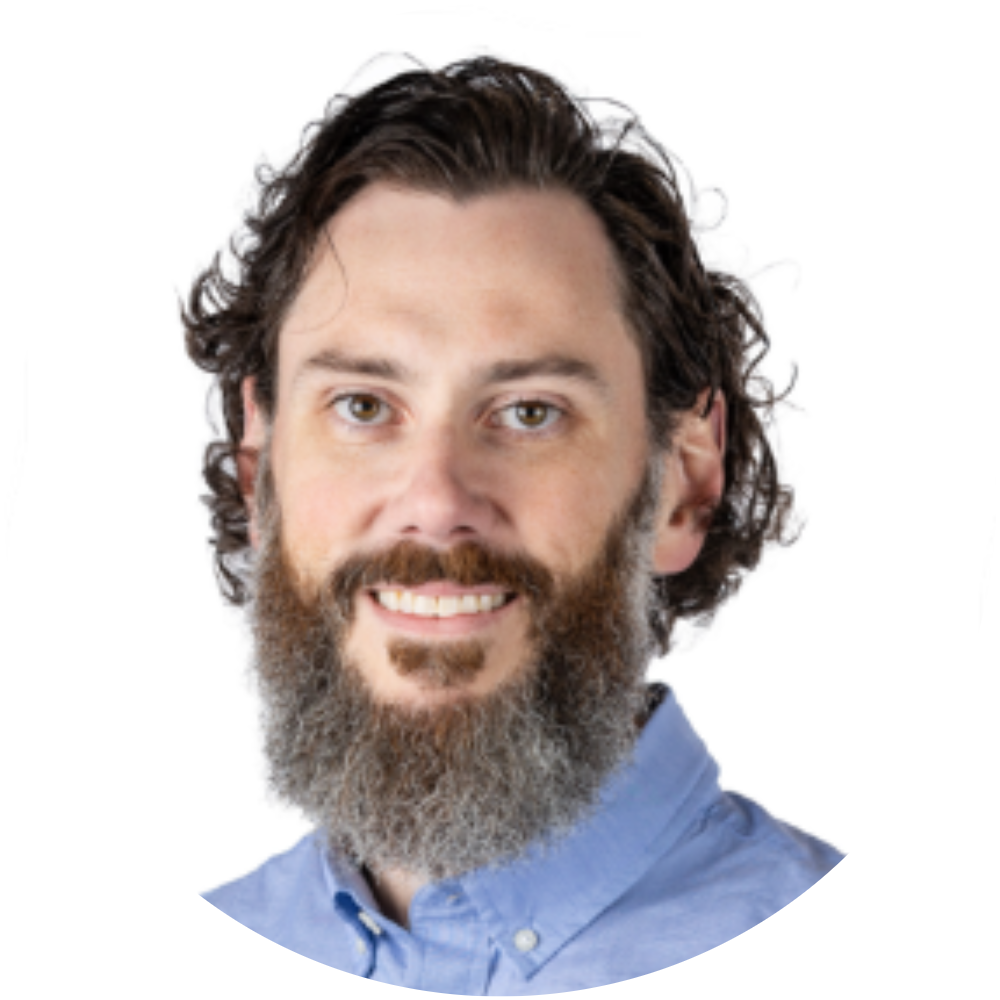 Portrait of a man with curly dark hair and a beard, wearing a light blue button-up shirt, smiling against a white background framed by a gold border.