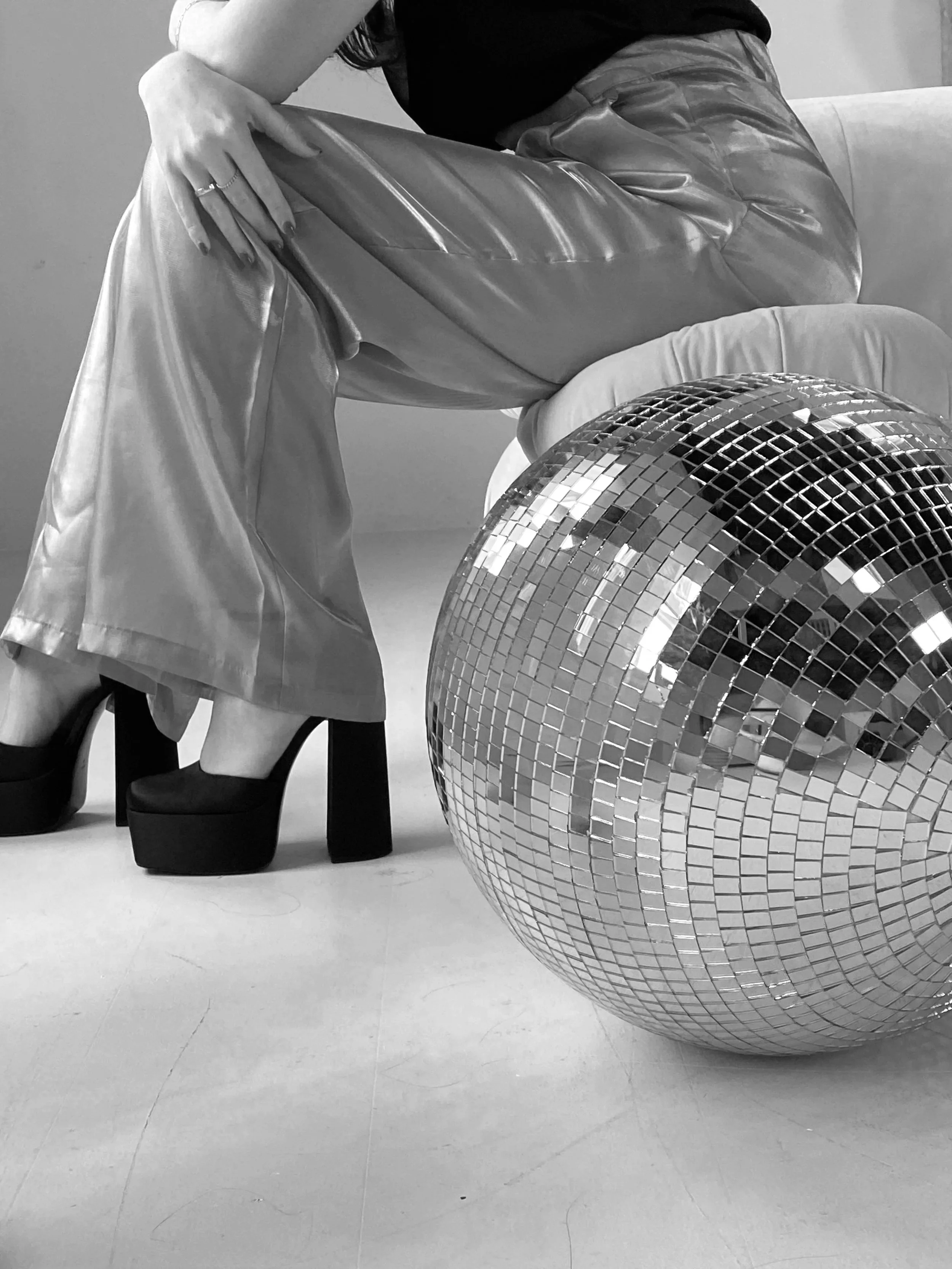A close up of a woman's legs and platform heels sitting on a chair next to a large disco ball.