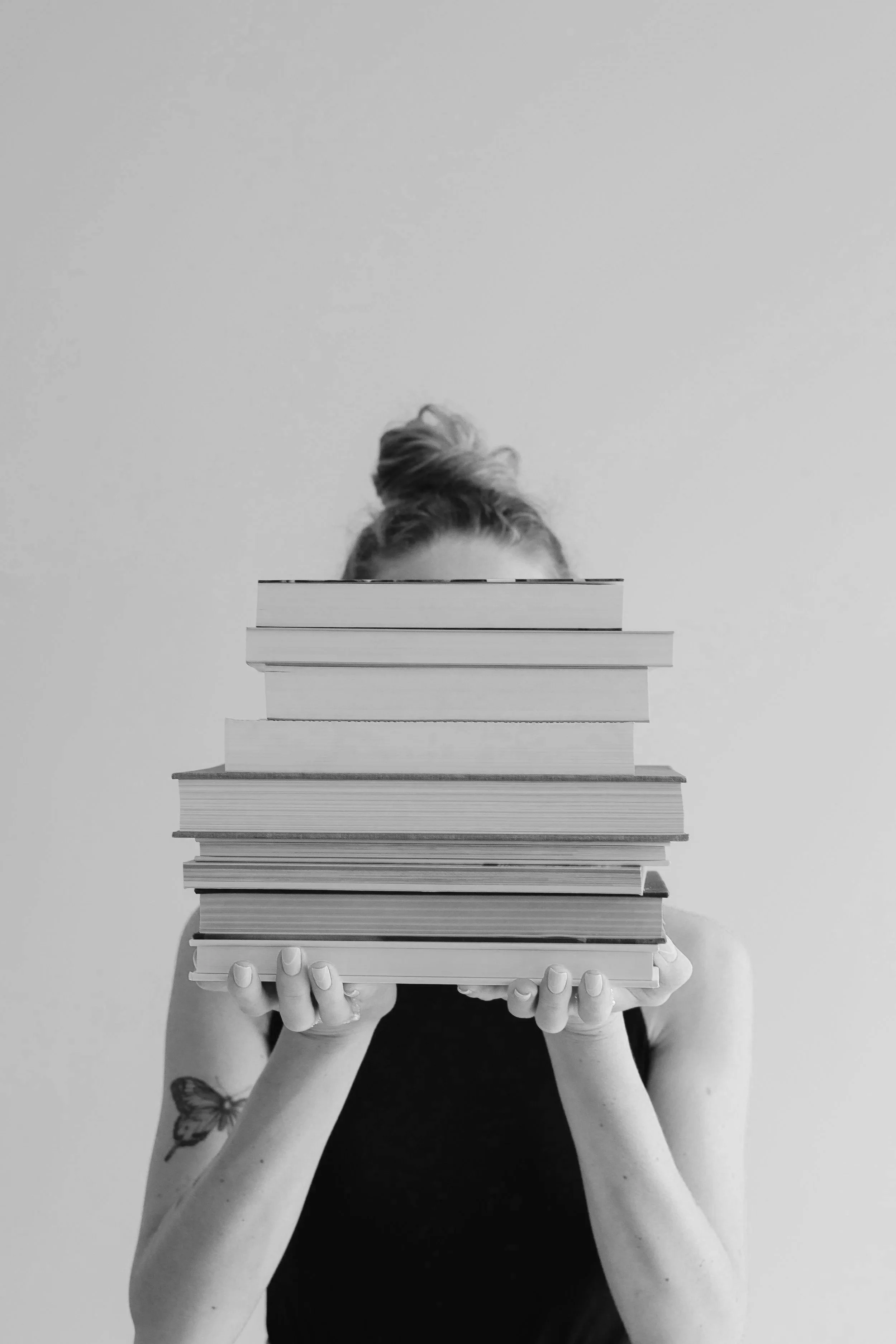 A woman holding a stack of books in front of her face.
