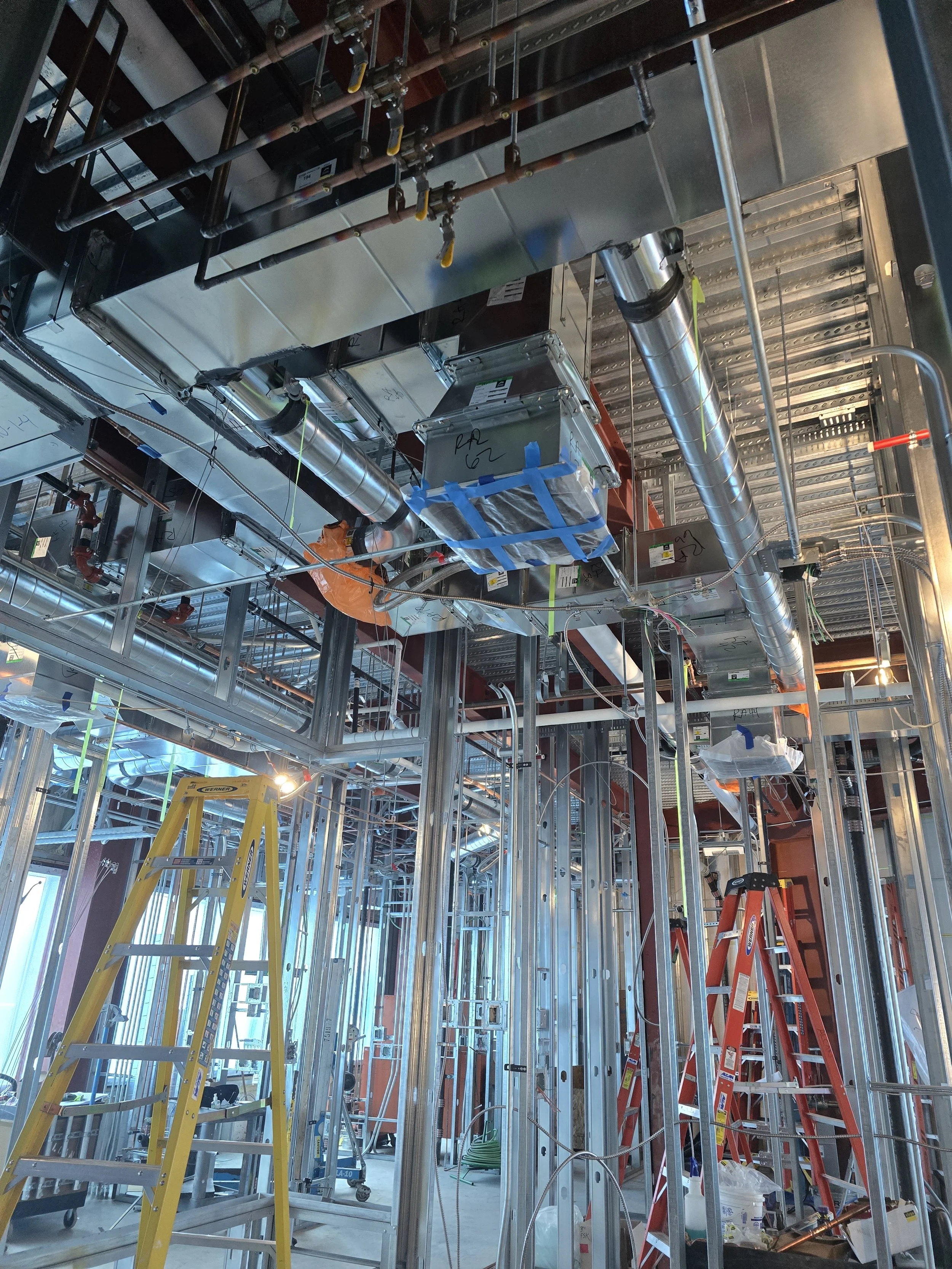 Construction site with metal framework, ladders, and piping in progress inside a building under construction.