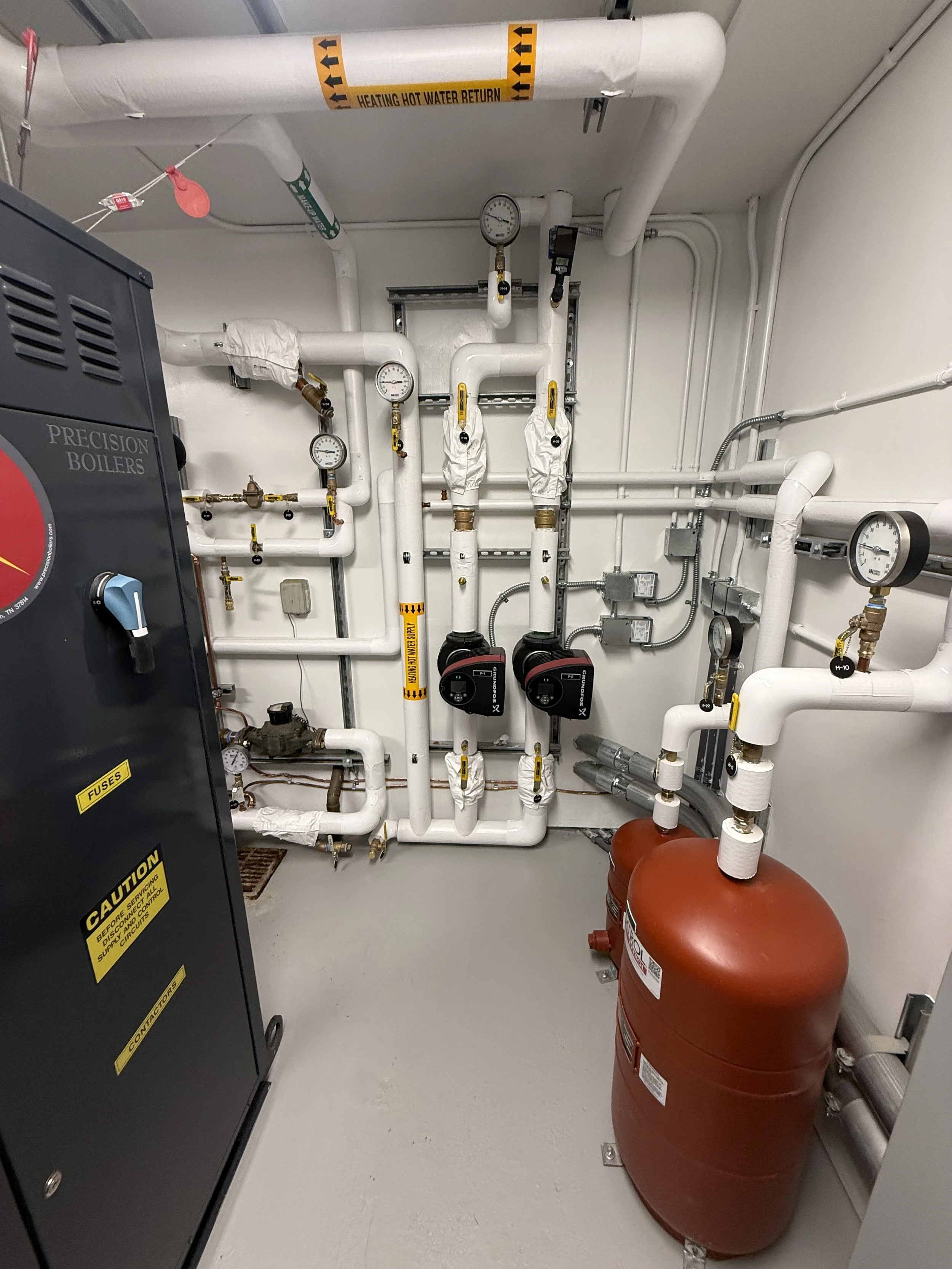 A utility room with white pipes, gauges, valves, and two red fire extinguishers