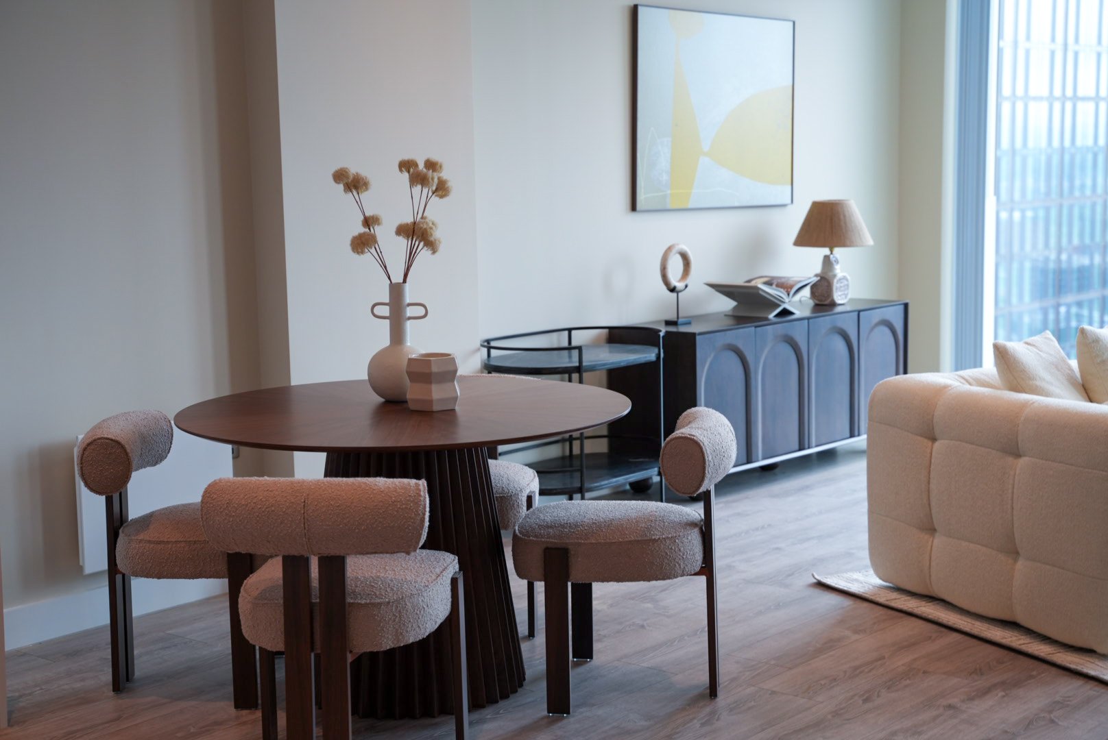 a wide shot of a living space with curved dining chairs, a walnut round table. 