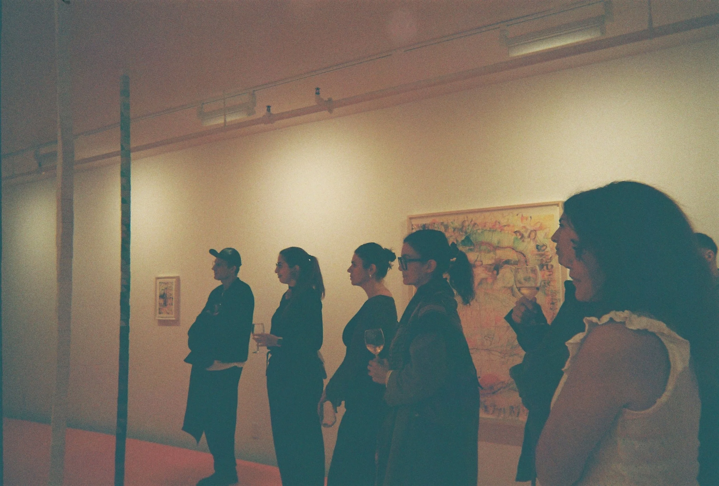 People standing in a line at an art gallery, holding glasses of wine, with artwork displayed on the wall behind them during a Dart Social Club experience.