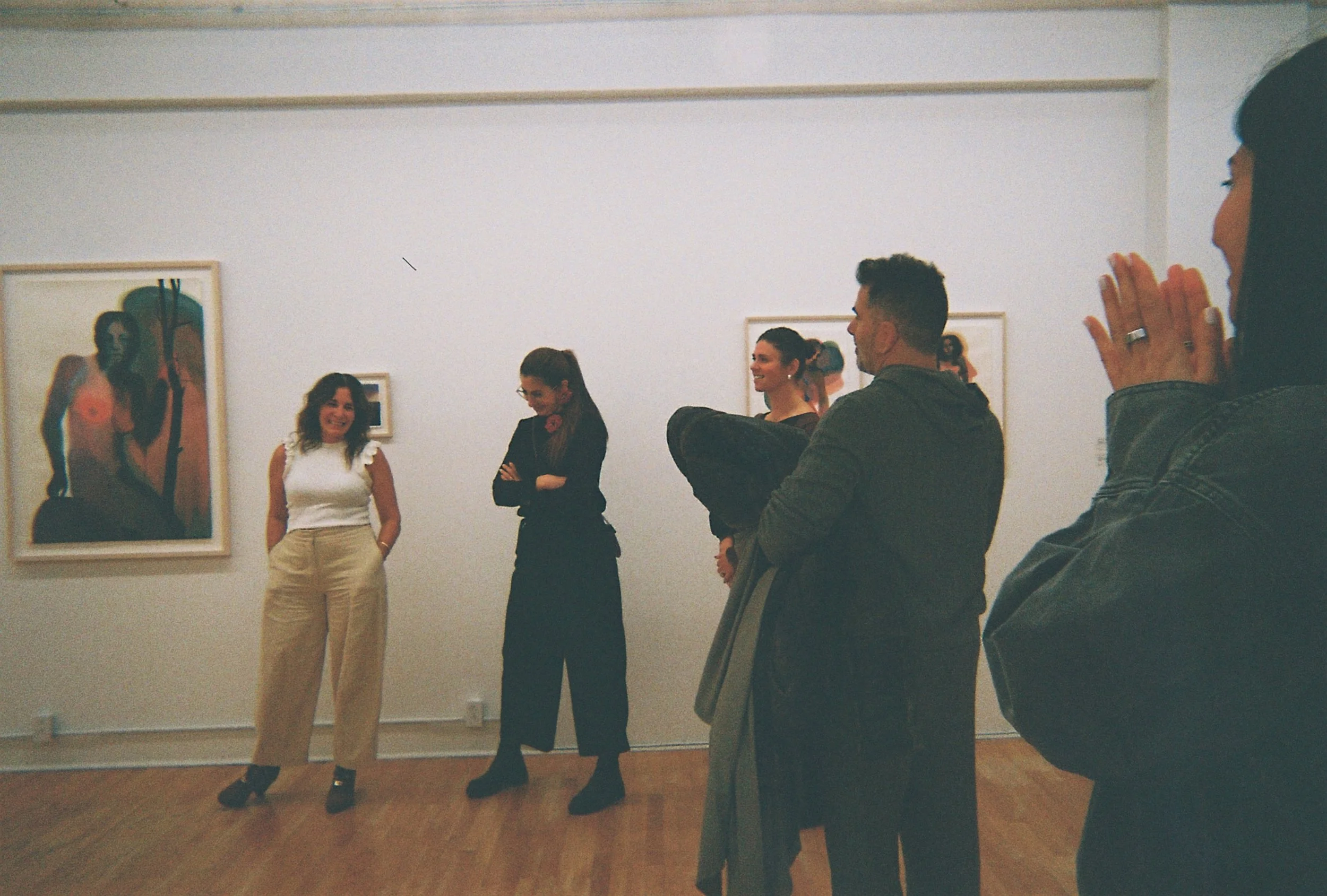 Group of people admiring artwork in an art gallery, including others standing in front of paintings on a white wall at a Dart Social Club experience.