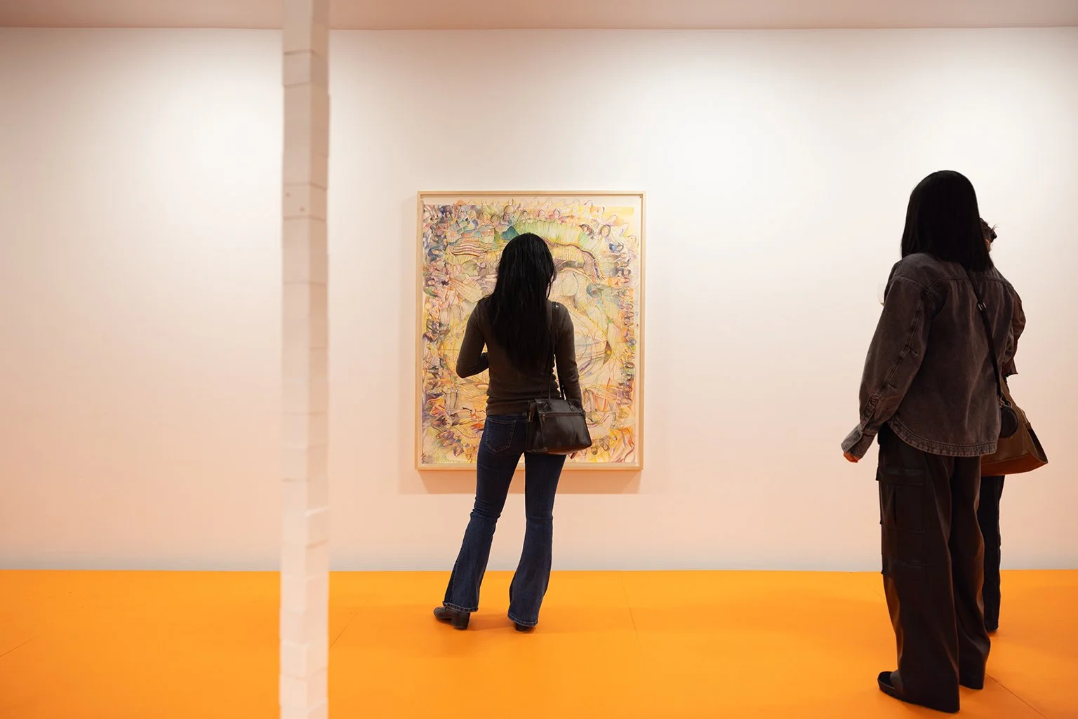 Three women viewing an abstract painting in an art gallery with white walls and an orange floor at a Dart Social Club experience.
