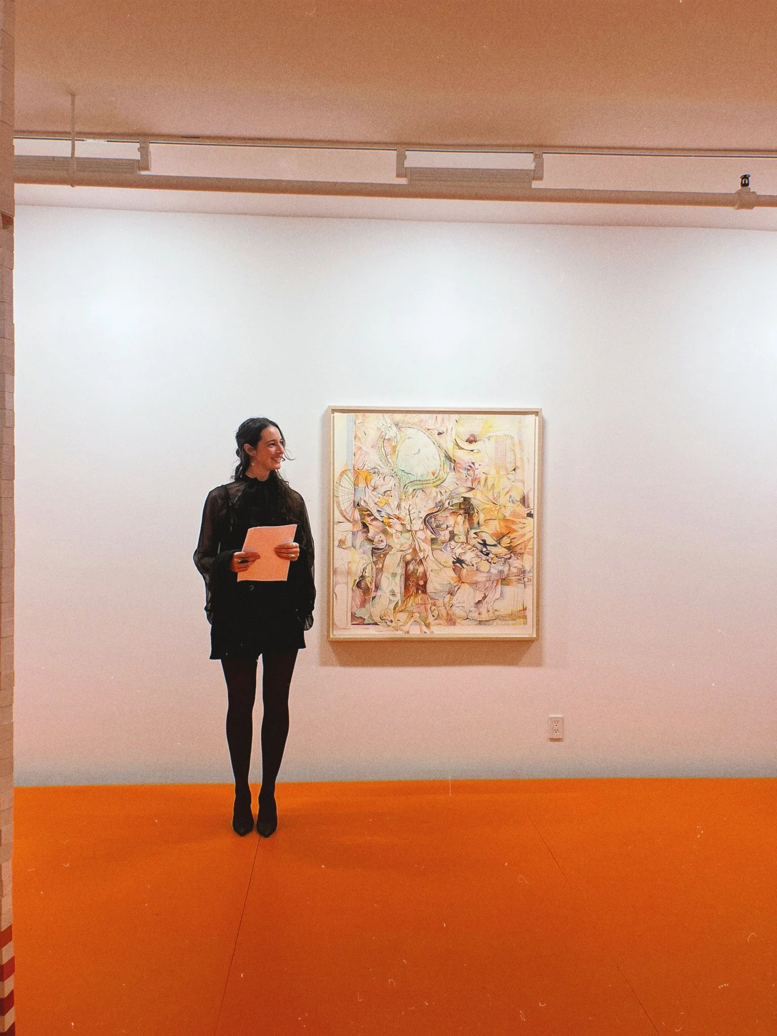 Sacha Sage, founder of Dart Social Club, standing in an art gallery, looking at a colorful abstract painting on a white wall.