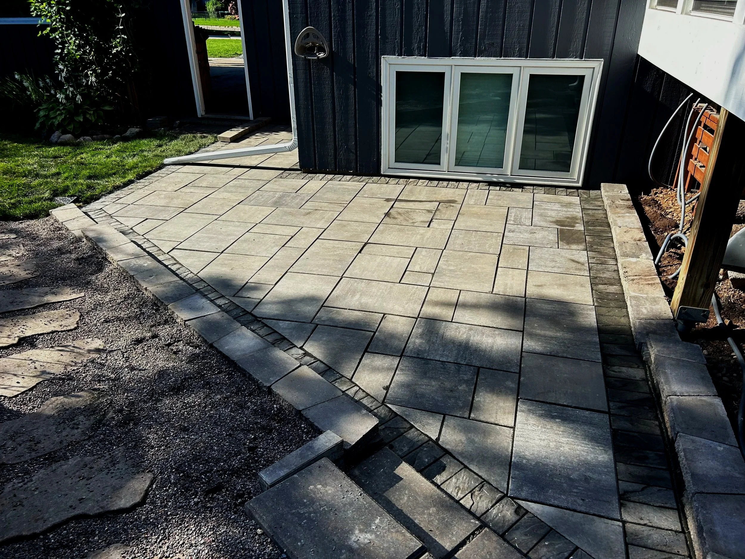 Newly paved concrete patio area next to a house with a sliding window, bordered by bricks and concrete blocks, with some dirt and gravel on the sides.