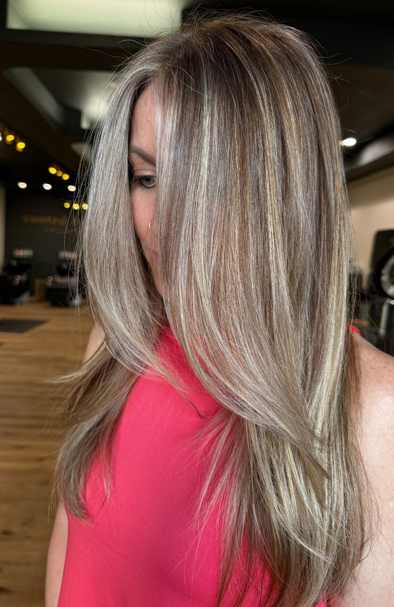 Close-up of a person with long, layered blonde hair, wearing a red top in a salon setting.