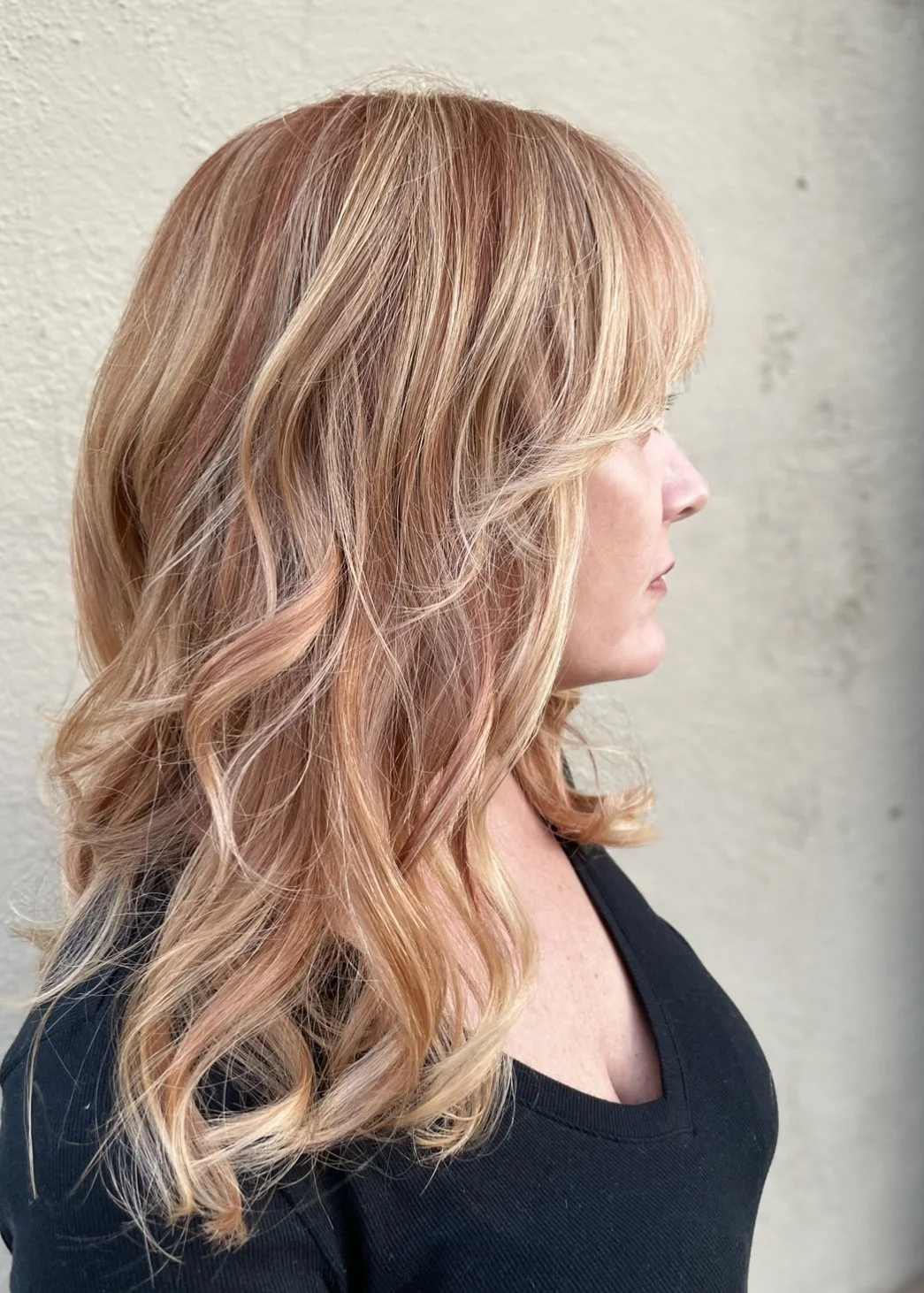Woman with long, wavy, strawberry blonde hair in profile view, wearing a black top.
