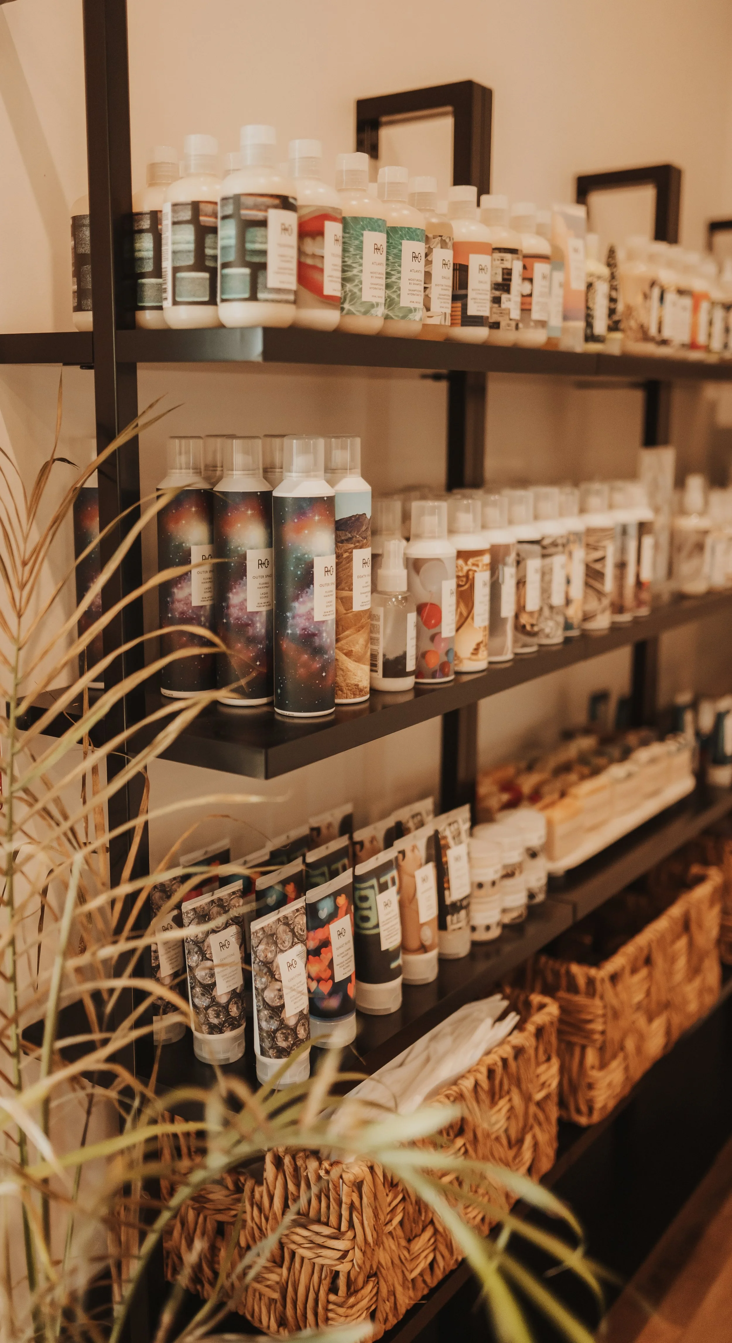 Shelves with various bottles of hair products and woven baskets, surrounded by a plant.