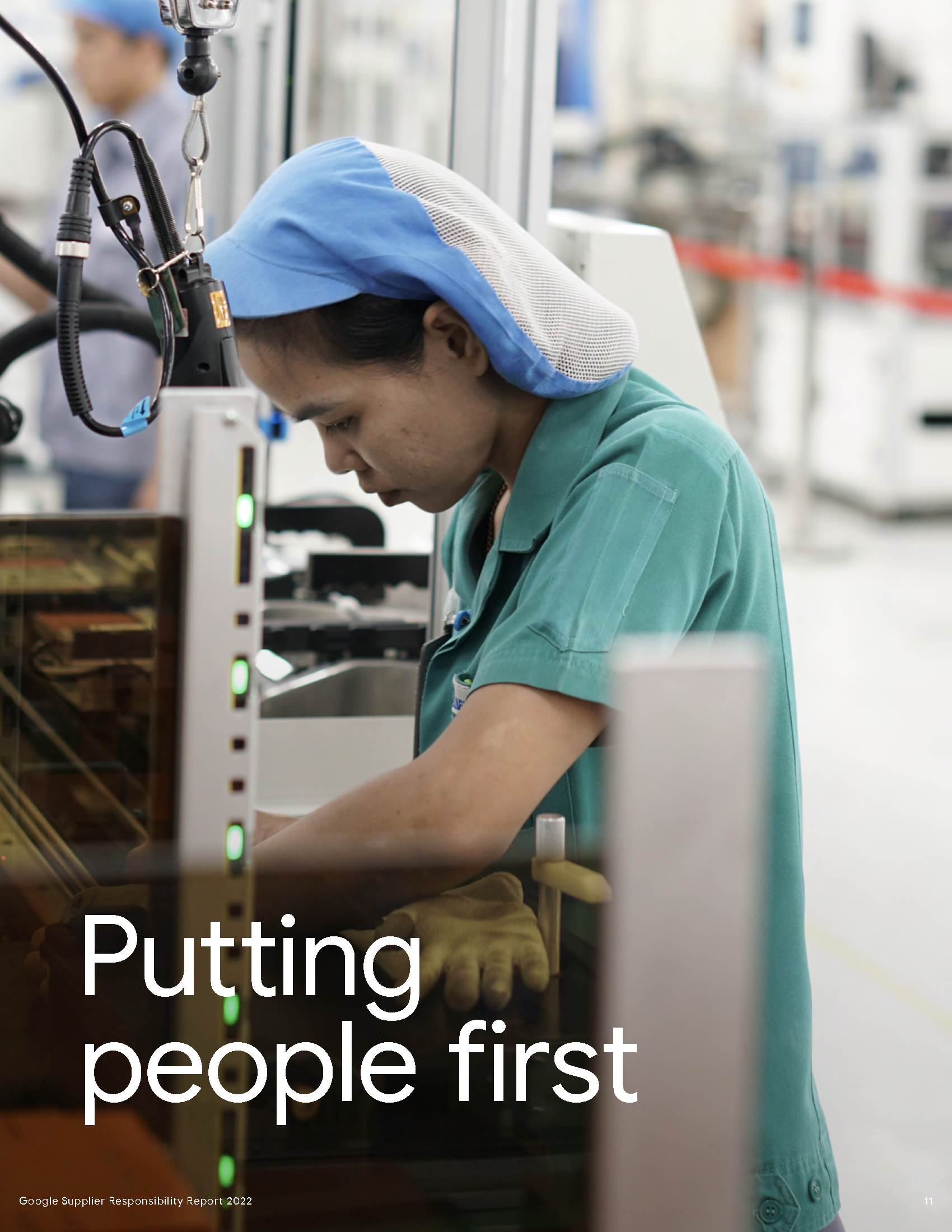 A worker in a factory wears a blue hairnet and green uniform, focused on a task near machinery.