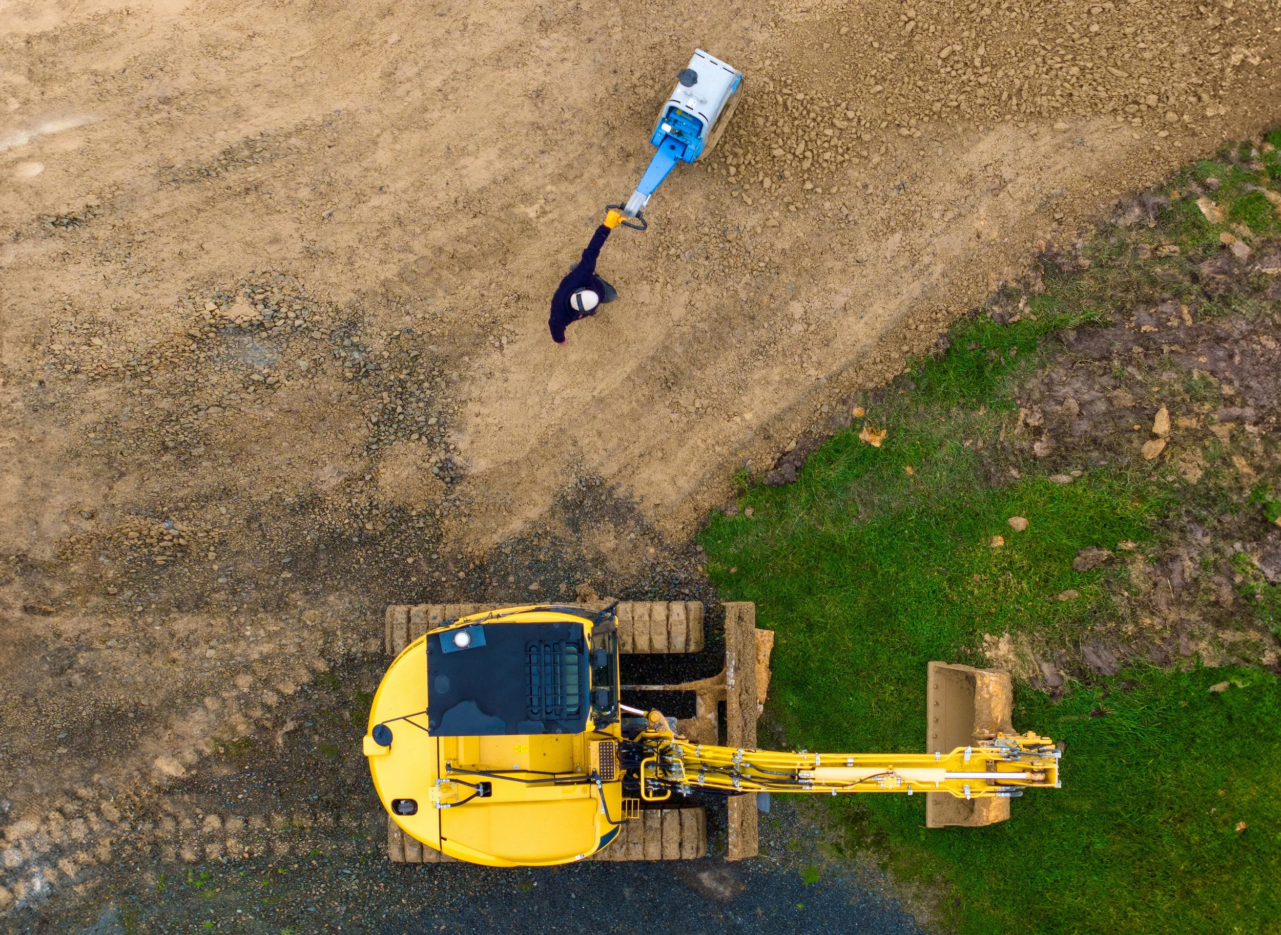 site worker using a plate compactor and excavator to form an accessway