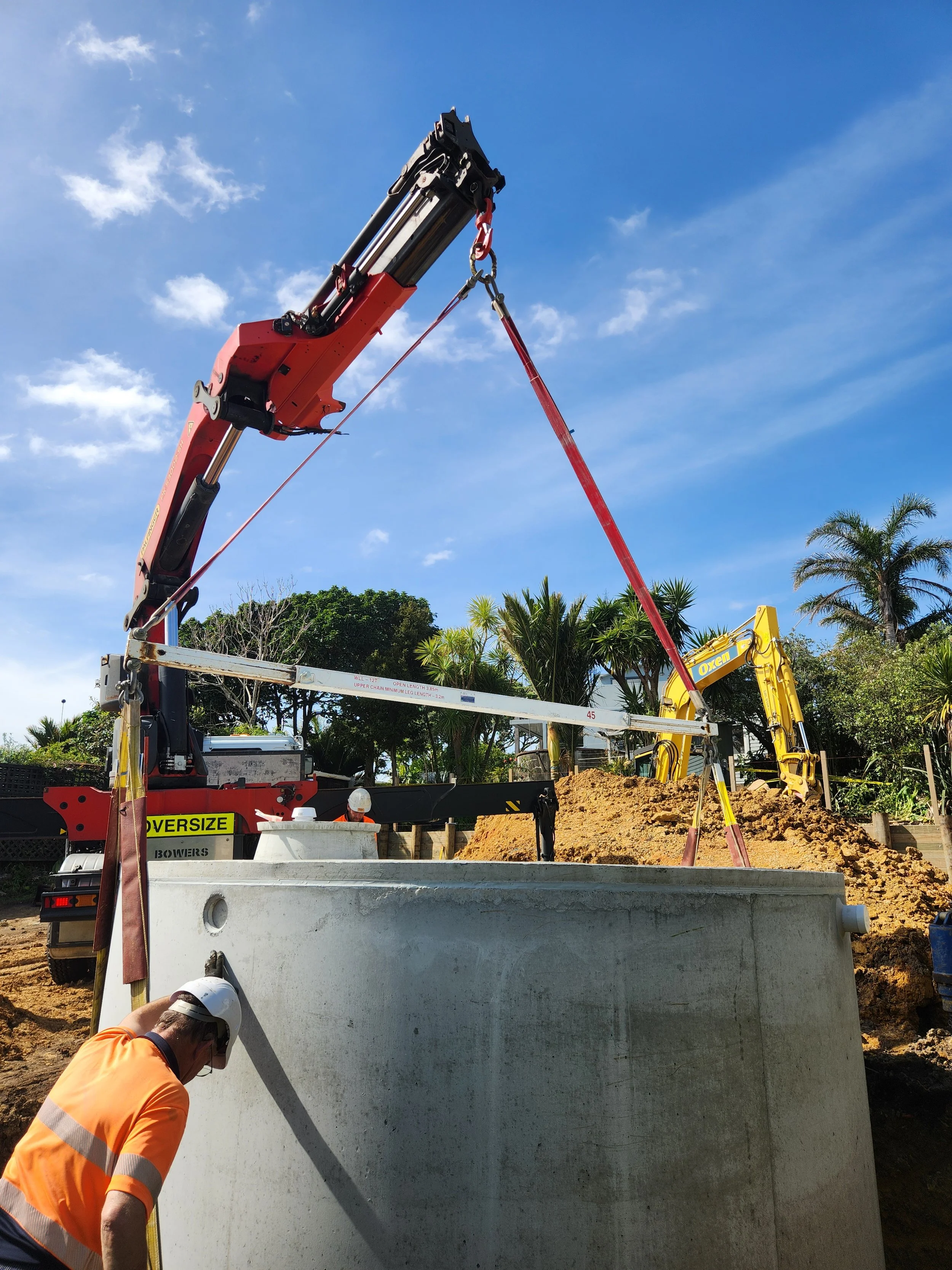 a concrete rainwater tank being lifted into an excavated hole by a hiab truck