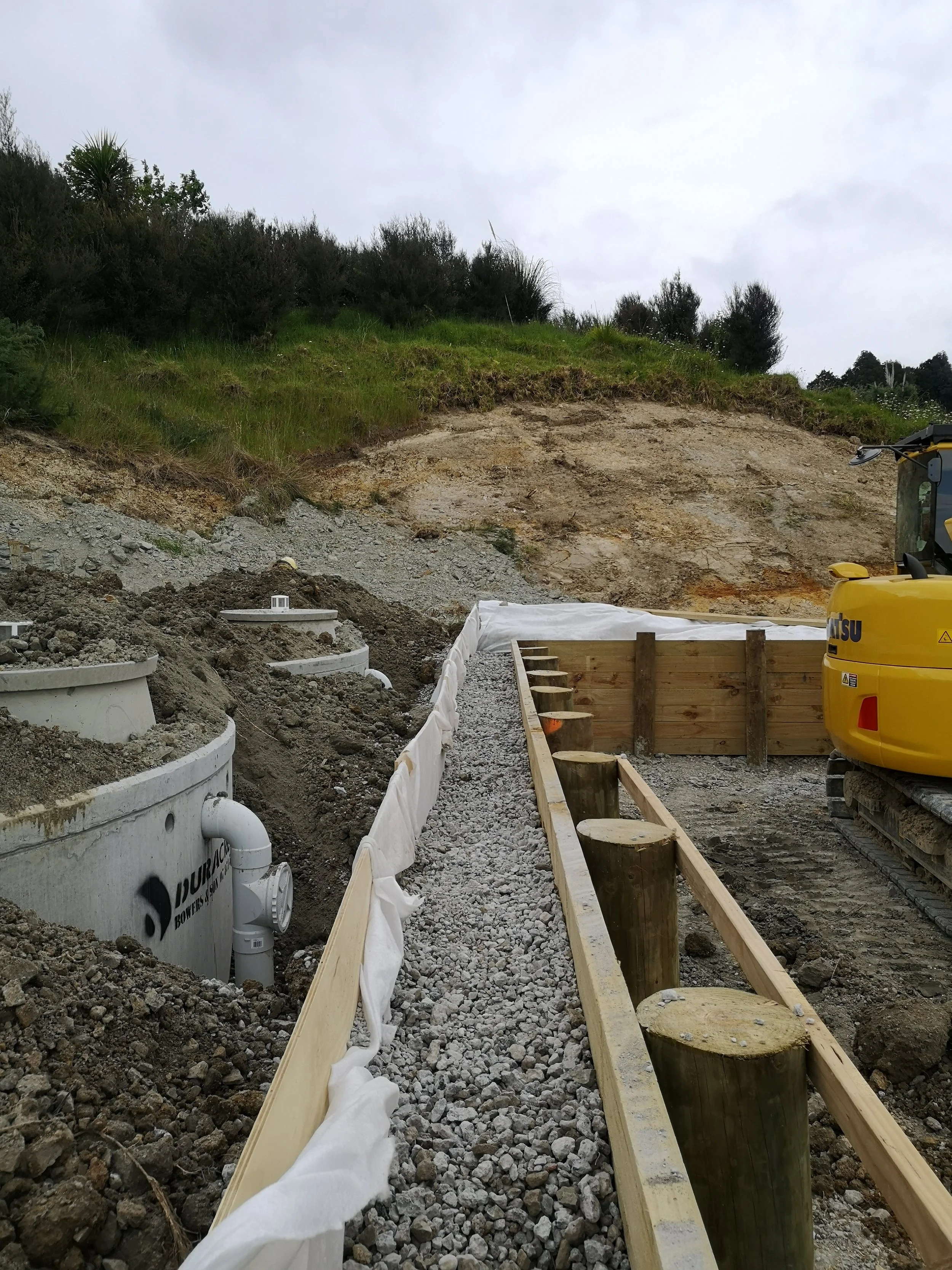 rainwater tanks being backfilled by an excavator next to a retaining wall with drainage channel