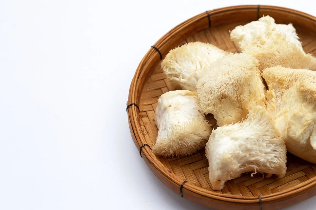 Pieces of fresh, white lion's mane mushrooms in a woven bamboo basket on a white background.