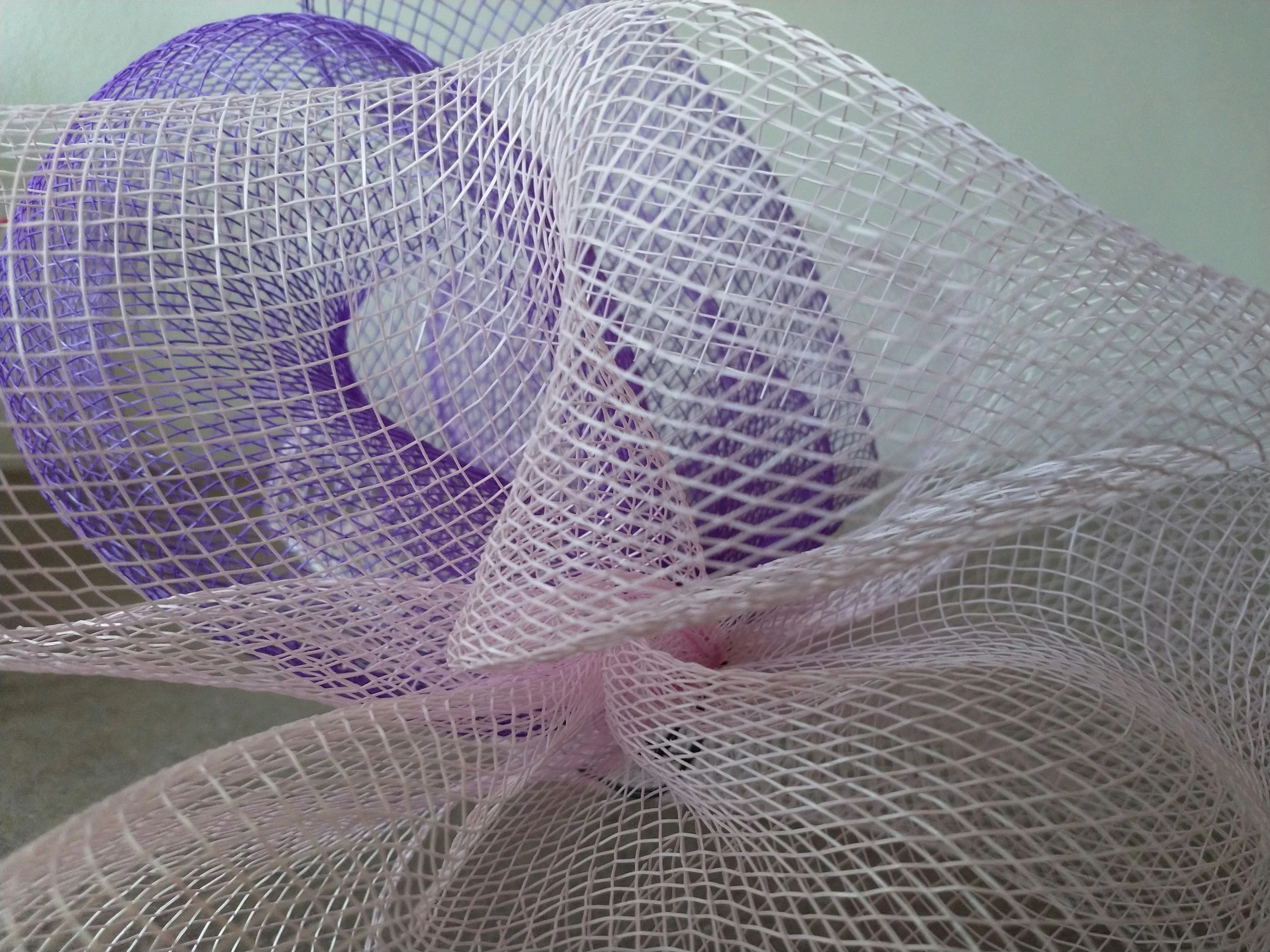 Close-up of decorative mesh fabric with purple and pink hues, featuring a grid pattern and swirling design.