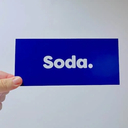 A person holding a gift voucher with the word "soda." written in white text.