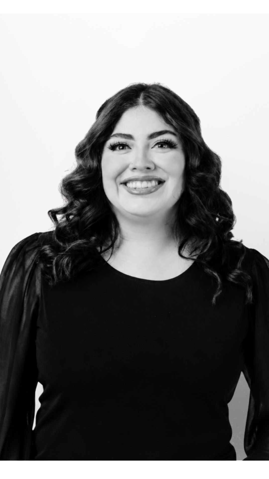Black and white portrait of a woman with dark wavy hair, smiling, wearing a dark top