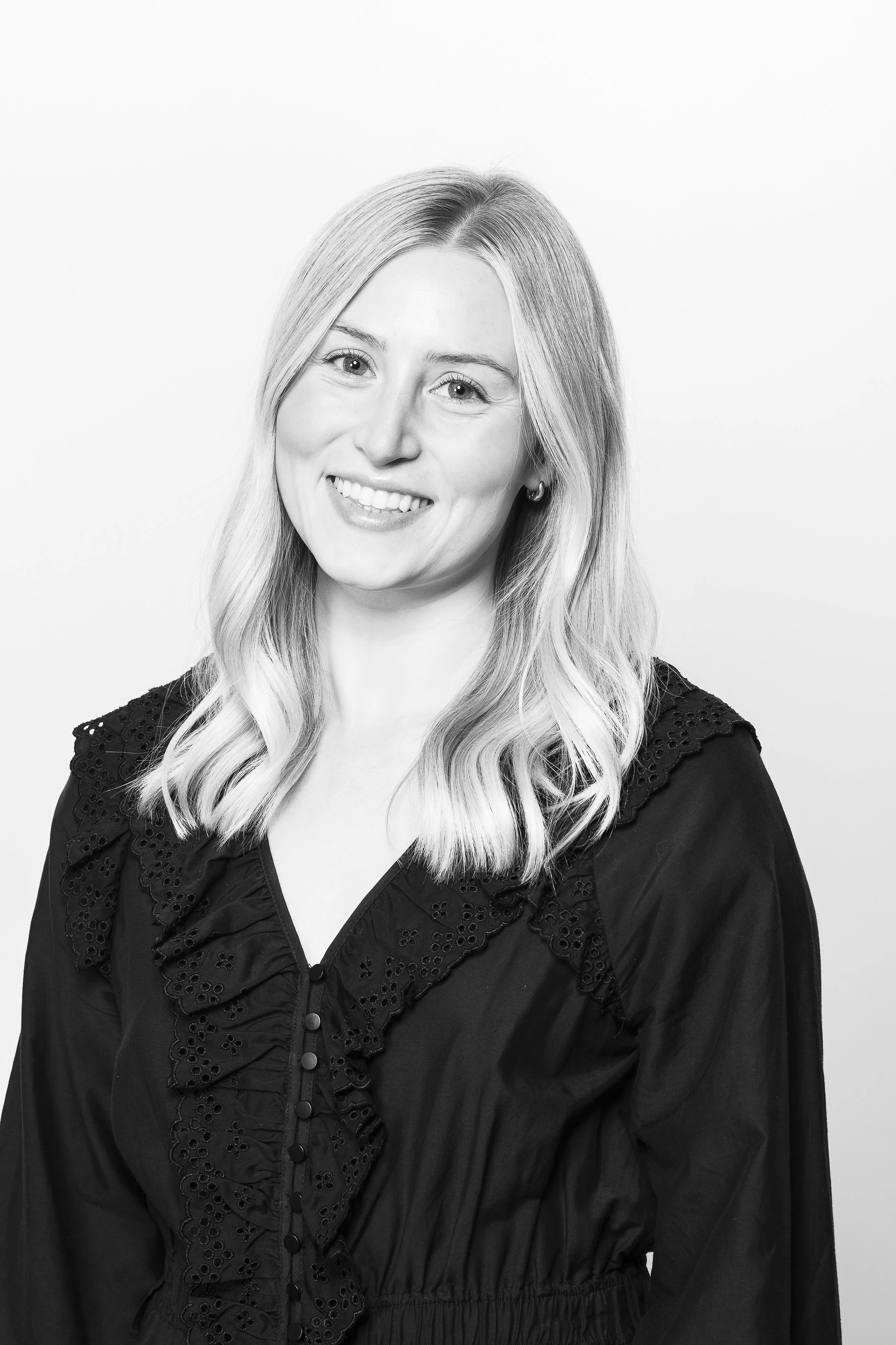 Black and white portrait of a woman with long blonde hair, smiling, wearing a button-up top with ruffled lace details on the front.