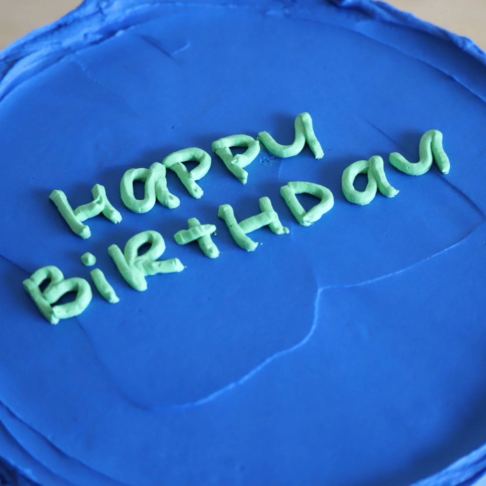 Vibrant blue cake with green frosting in the shape of 'Happy Birthday' words.