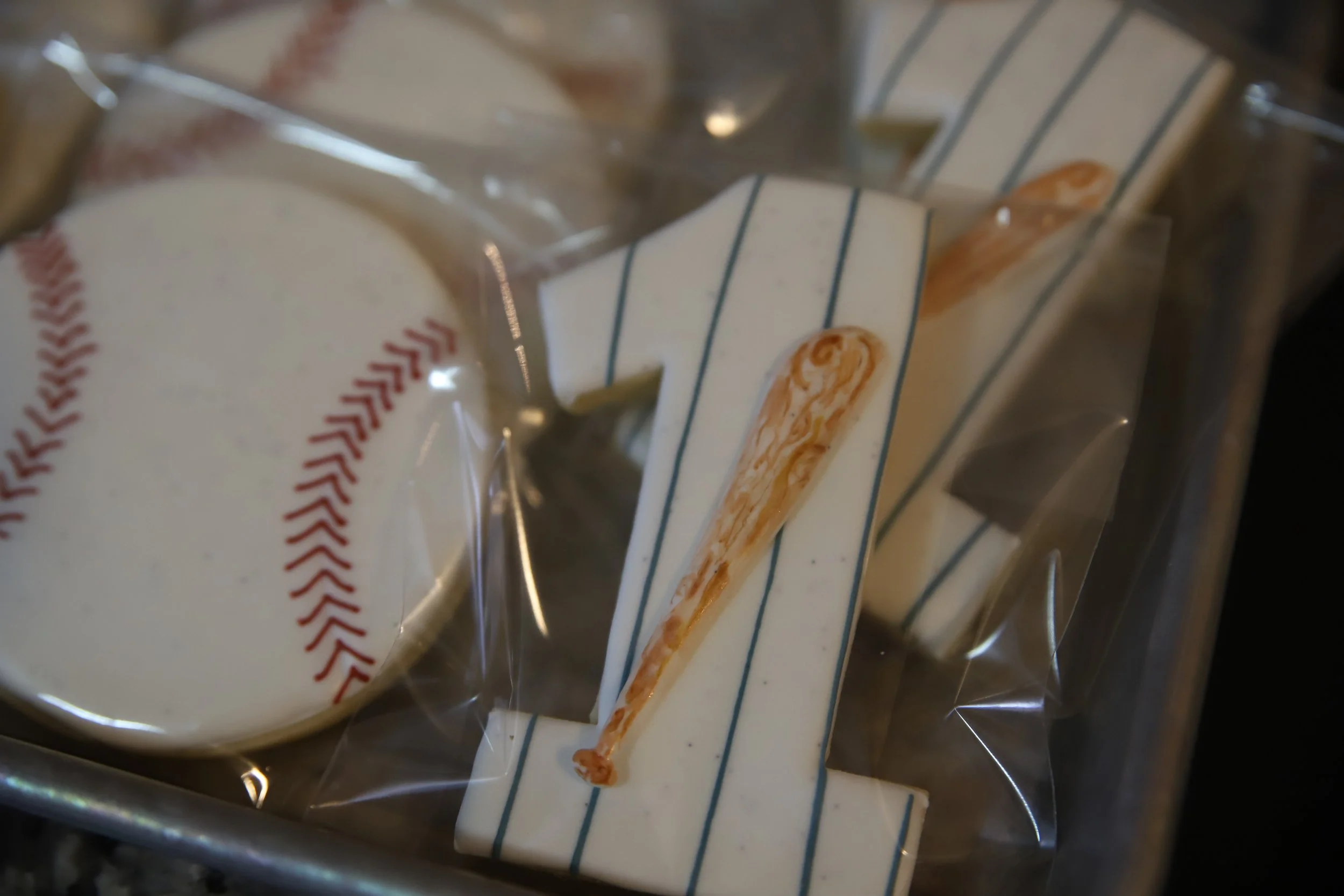 Various packaged cookies, including a baseball with red stitching and a number "1" with a small wooden bat on it, inside a transparent plastic bag.