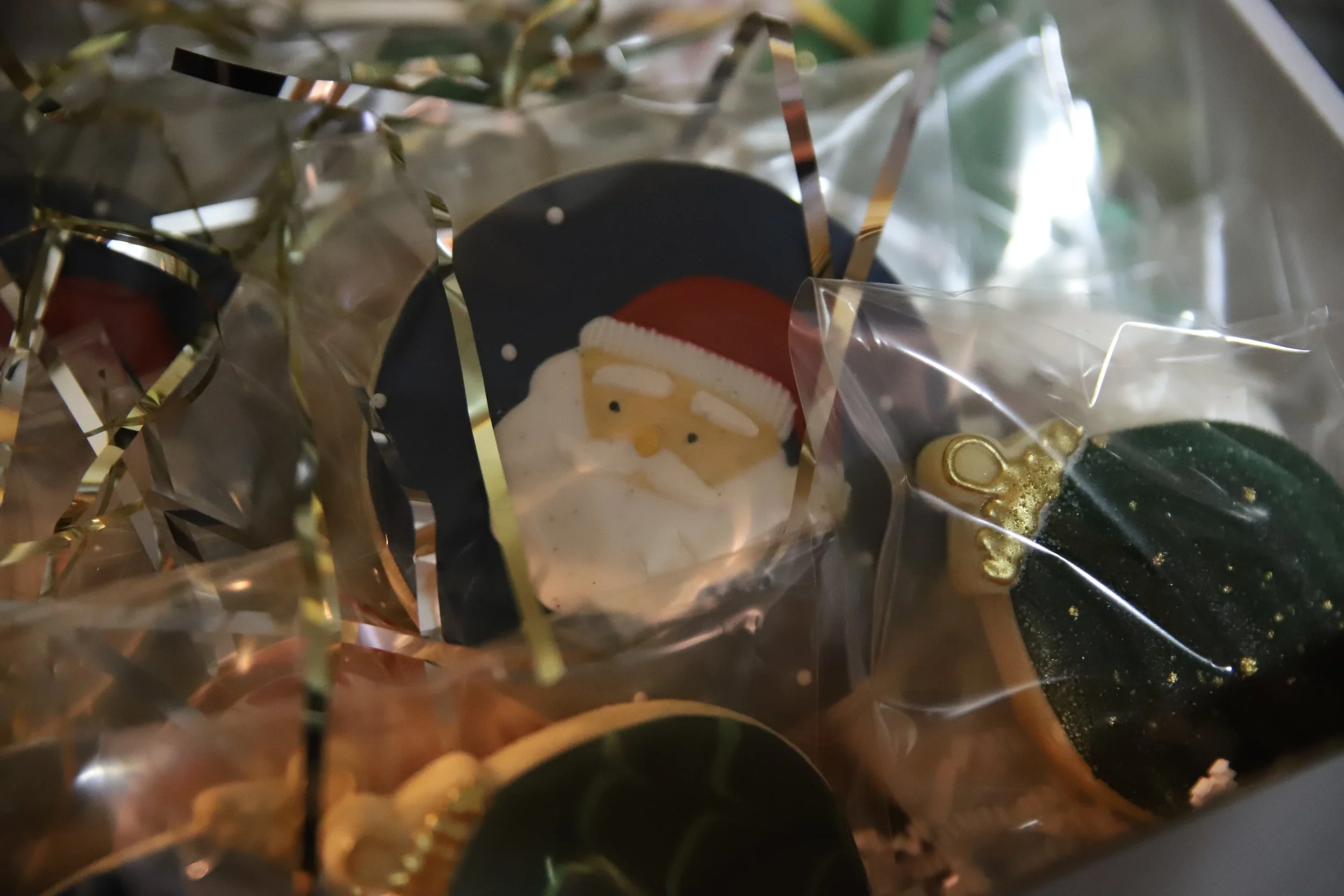 A close-up of a box of cookies gift wrapped in metallic gold and silver ribbon with a festive cookie featuring santa wearing a red hat and scarf.