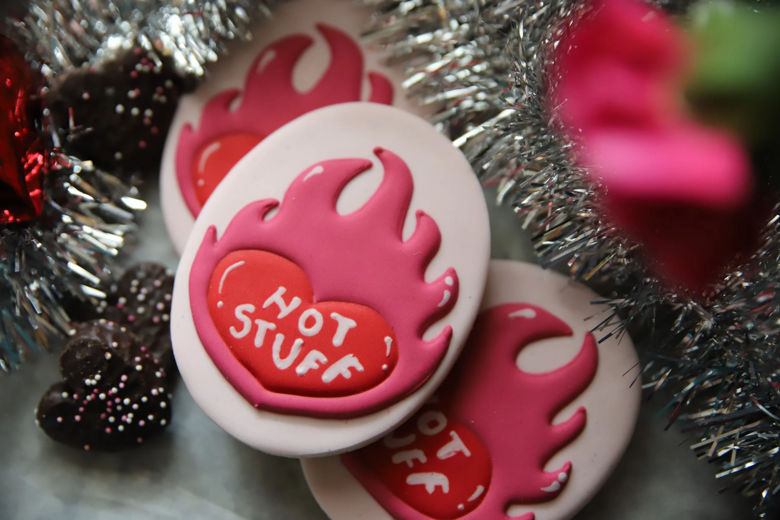 Close-up of pink and white cookies with a flame design and a message that says 'Hot Stuff' surrounded by silver tinsel and sprinkles.