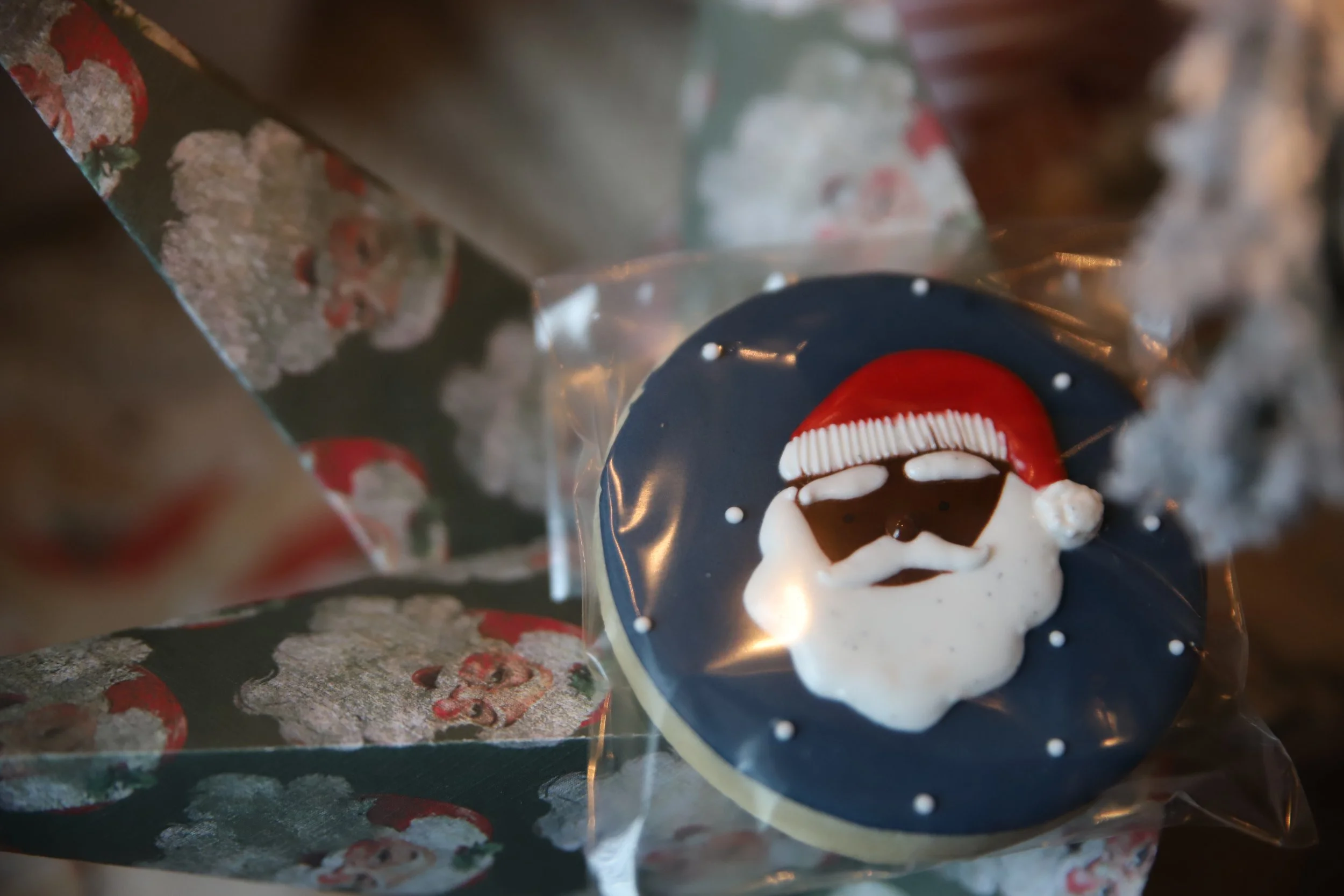 A decorated Christmas cookie with a Santa Claus face on a shiny dark blue surface, surrounded by silver ribbon, in a close-up view.