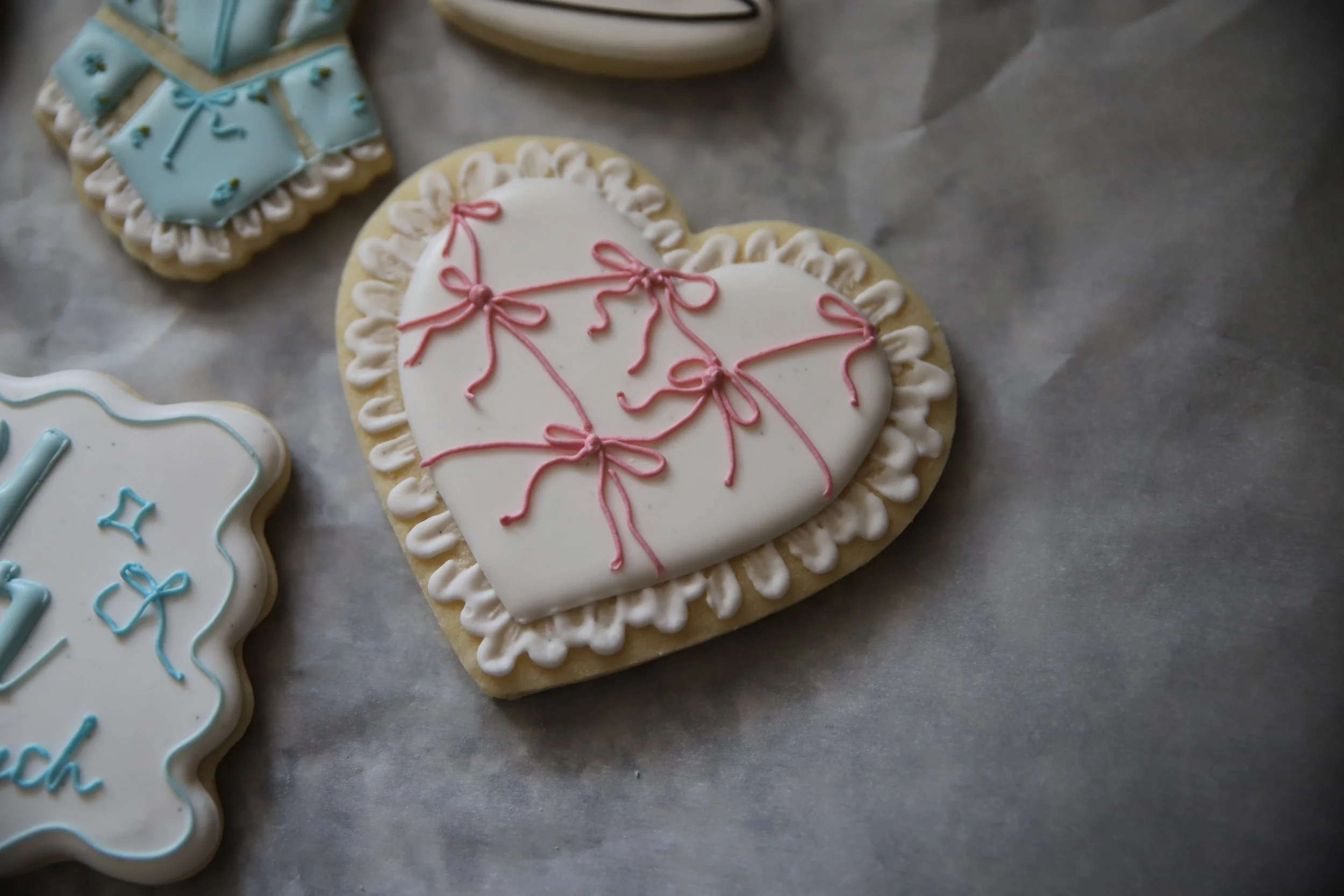 Heart-shaped cookies decorated with white and pink icing, with the pink icing forming bows and lines, and blue icing on other cookies to the left.