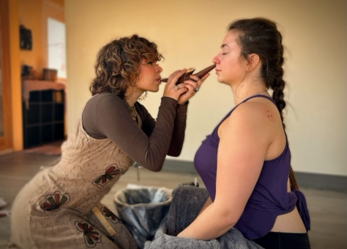 A practitioner administering sacred hapé using a kuripe during ceremony, offering grounding, intention, and mindful support in a healing space at Ahavah Gardens.