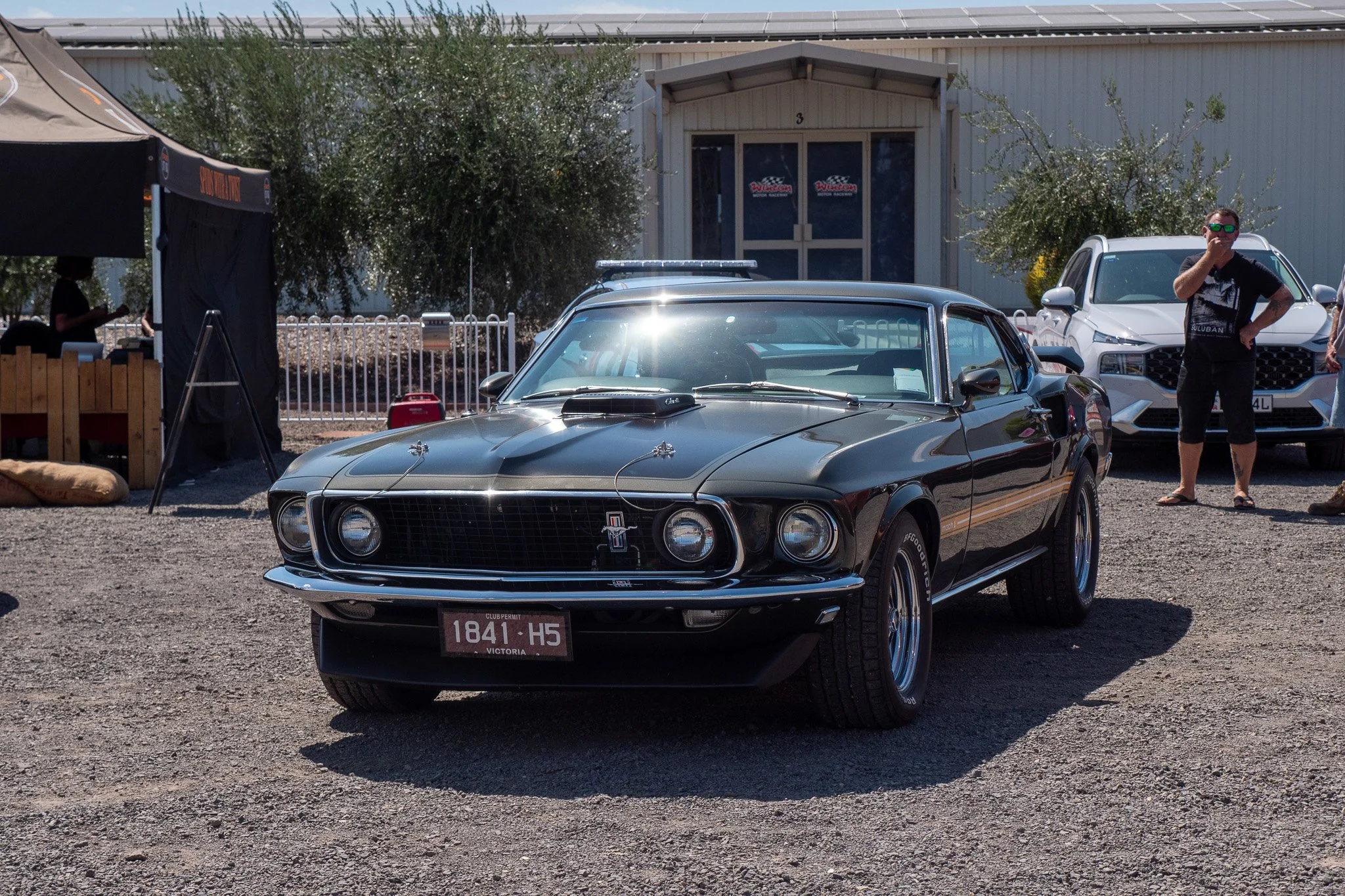 A black vintage Ford Mustang car parked outdoors with people nearby and a building in the background.