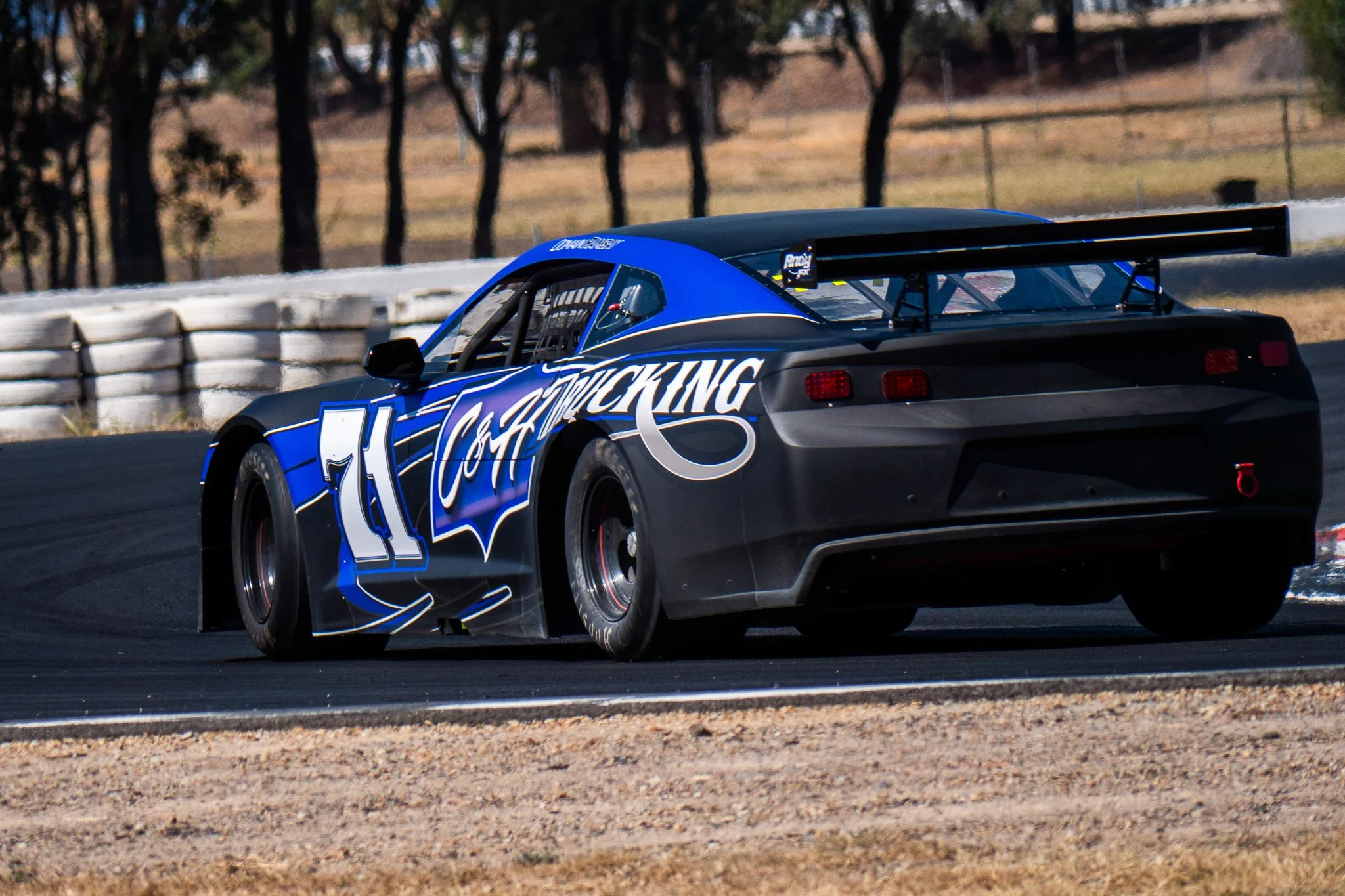 A race car with the number 11 on the side, painted in black and blue, is on a race track during daytime.