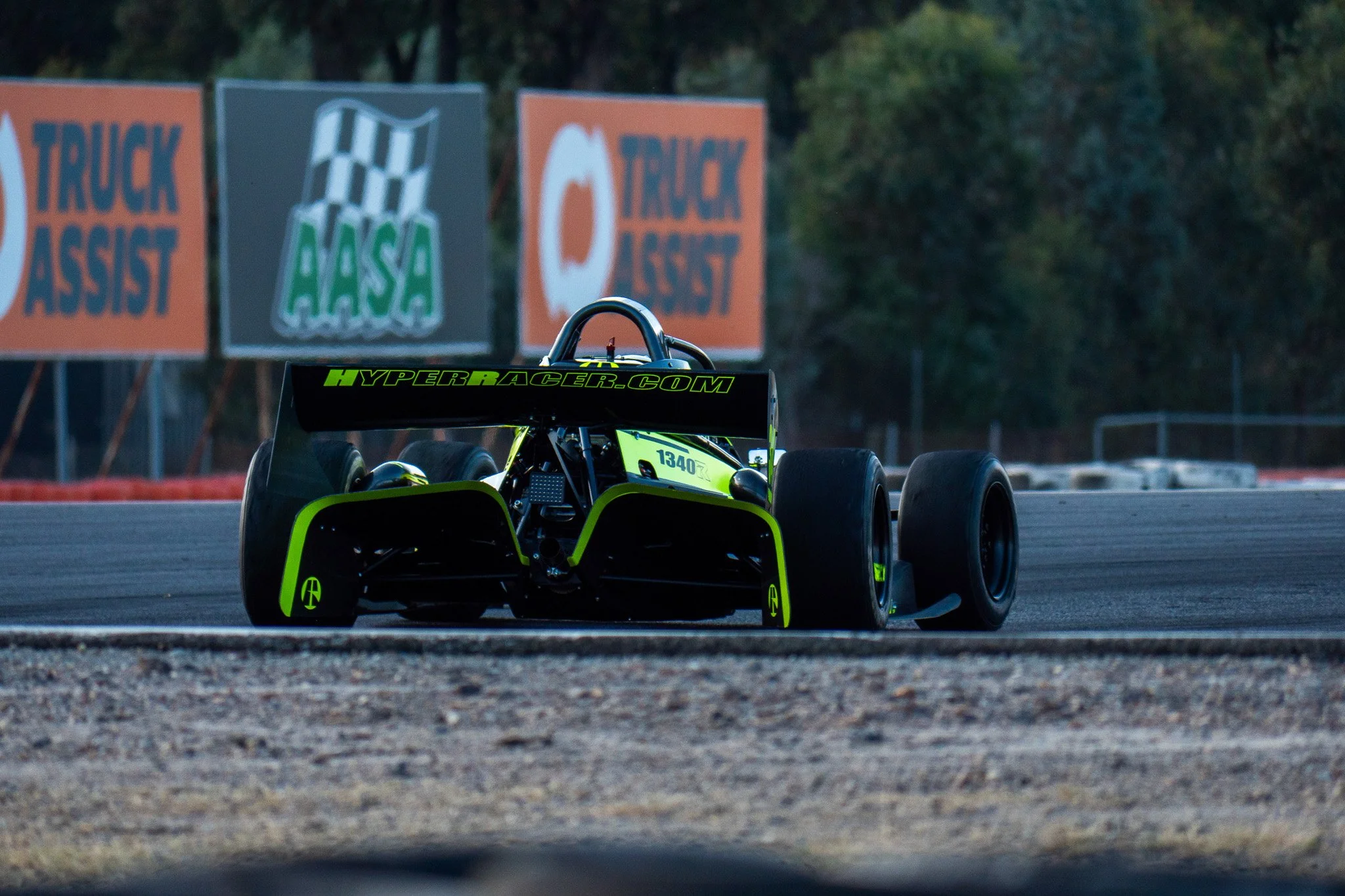 A race car on a track during daylight with promotional banners in the background.