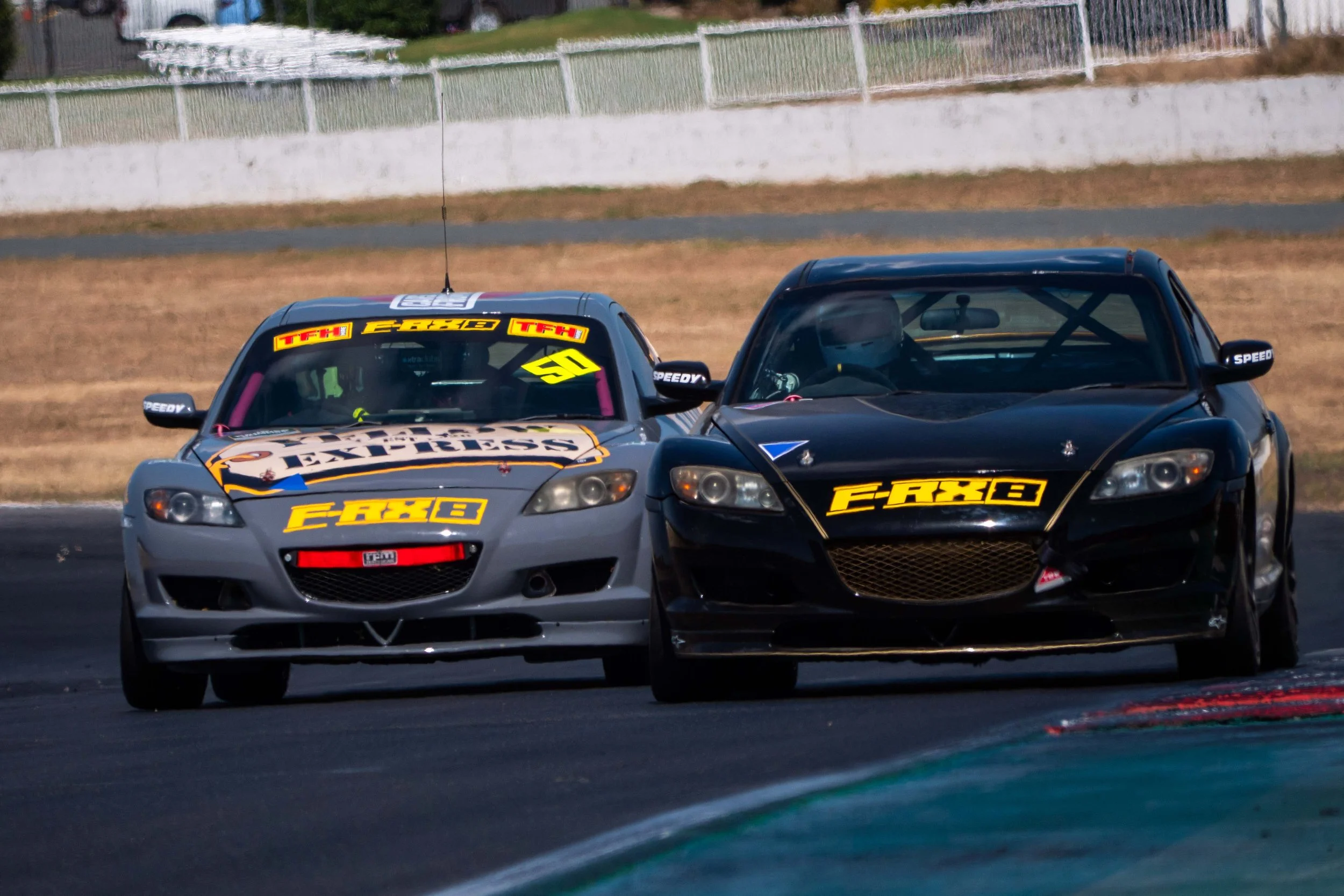 Two racing cars on a track, one silver with logos and the other black with logos, competing closely in a race.