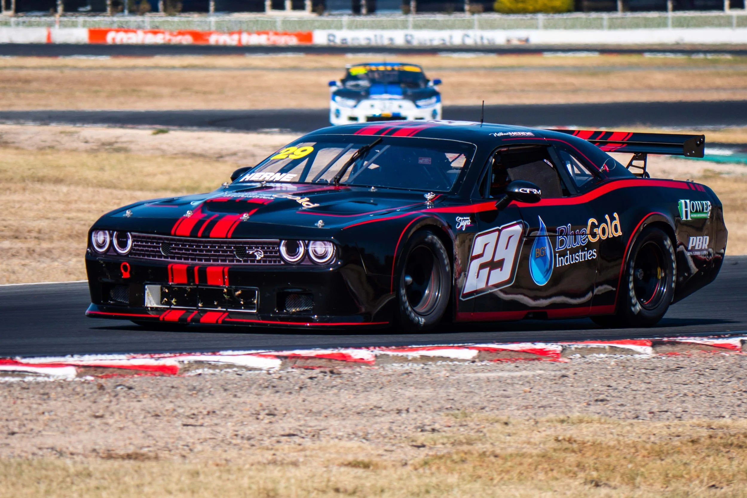 A black race car with red stripes, number 29, on a race track, with another car in the background.