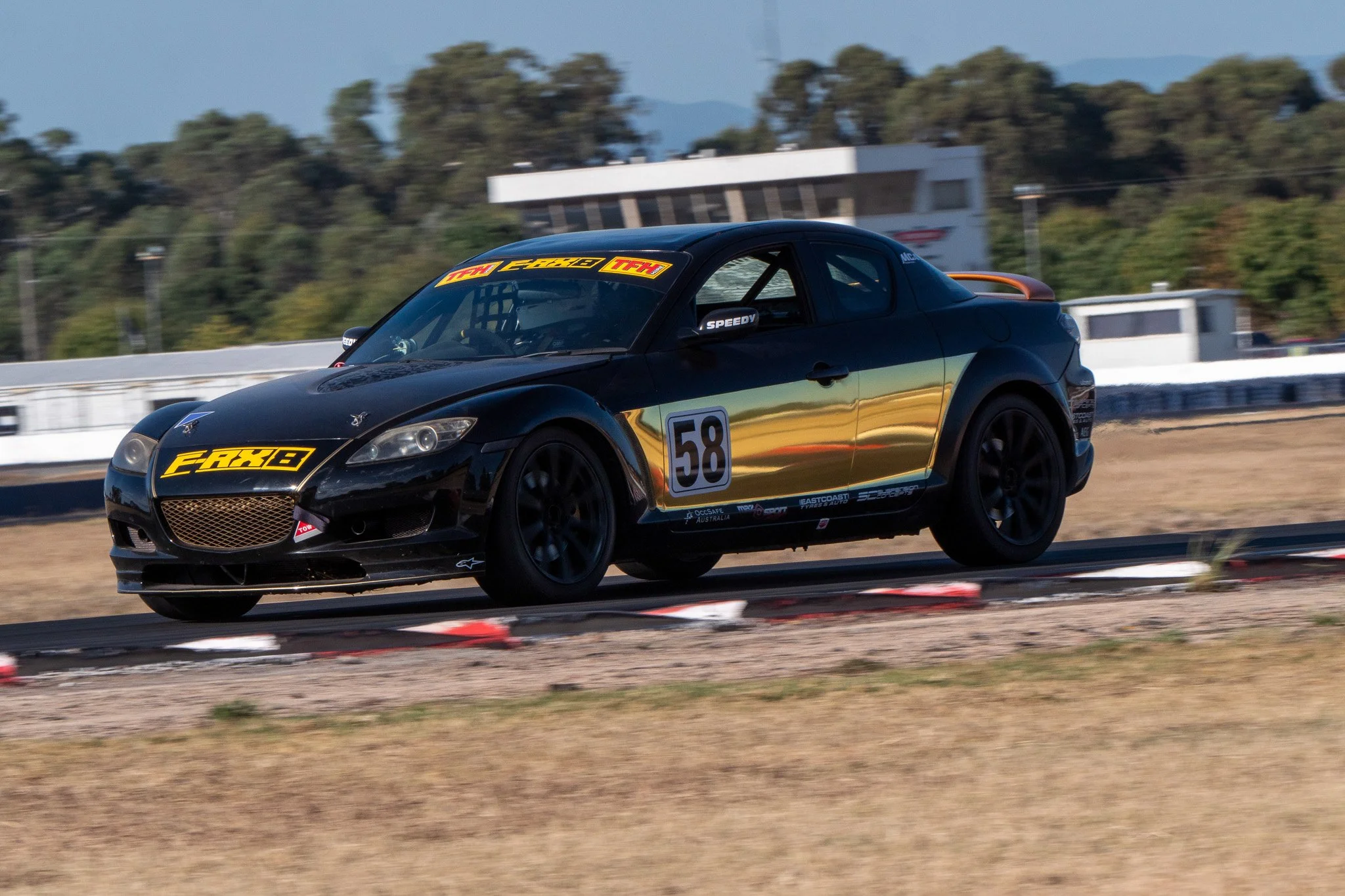 Black race car with yellow decals on a race track.