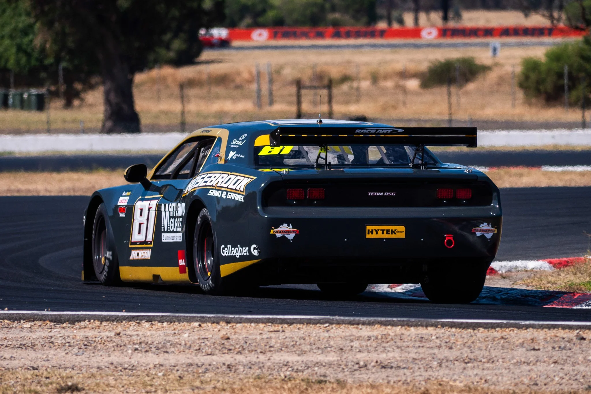 A race car on a track, with a large rear wing, black with yellow accents, the number 81, and various sponsor logos, including Gallagher and Hytek.