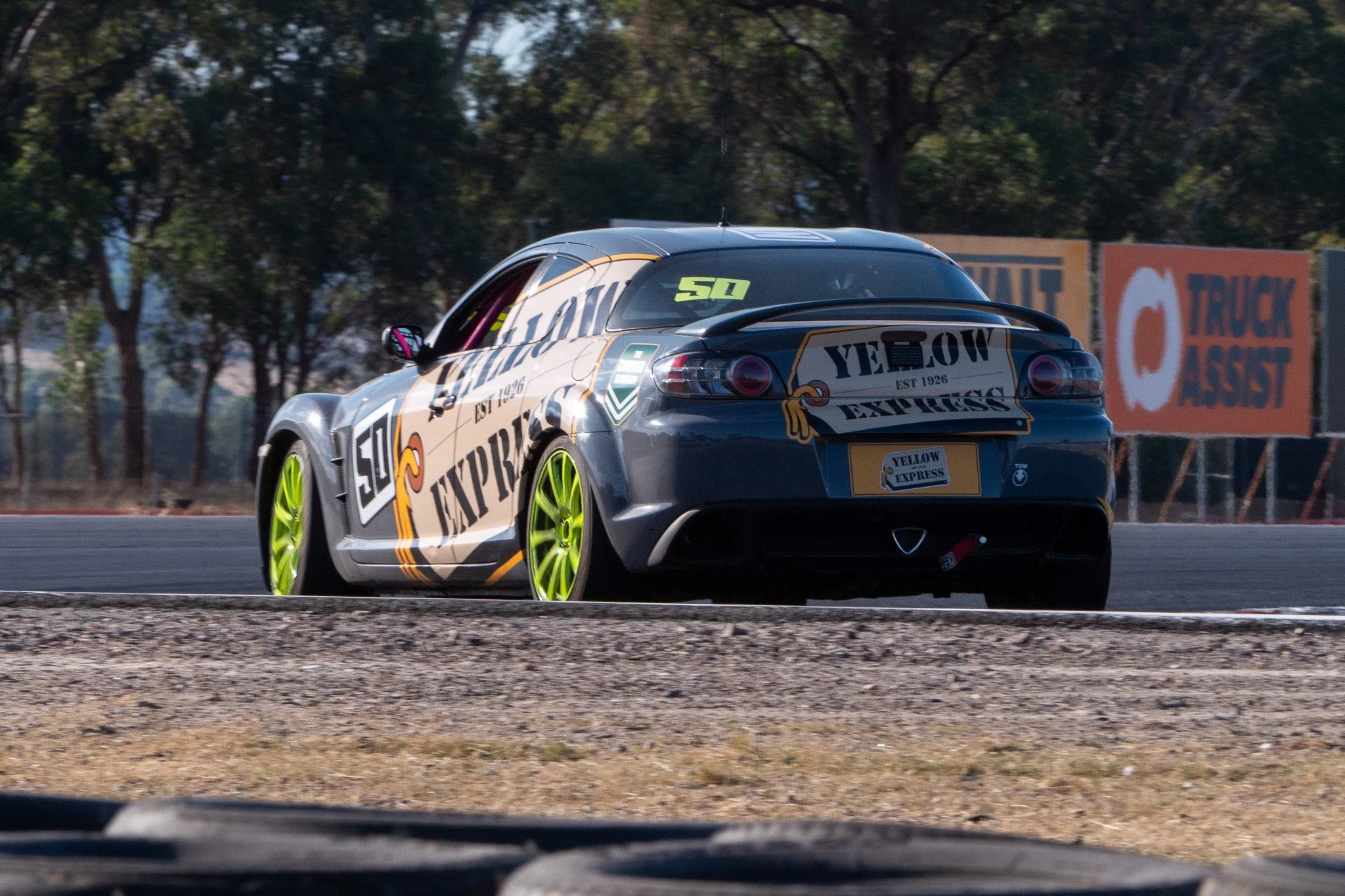 A race car with yellow wheels on a racetrack, bearing the logo 'Yellow Express' and other racing decals, in a sunny outdoor setting.