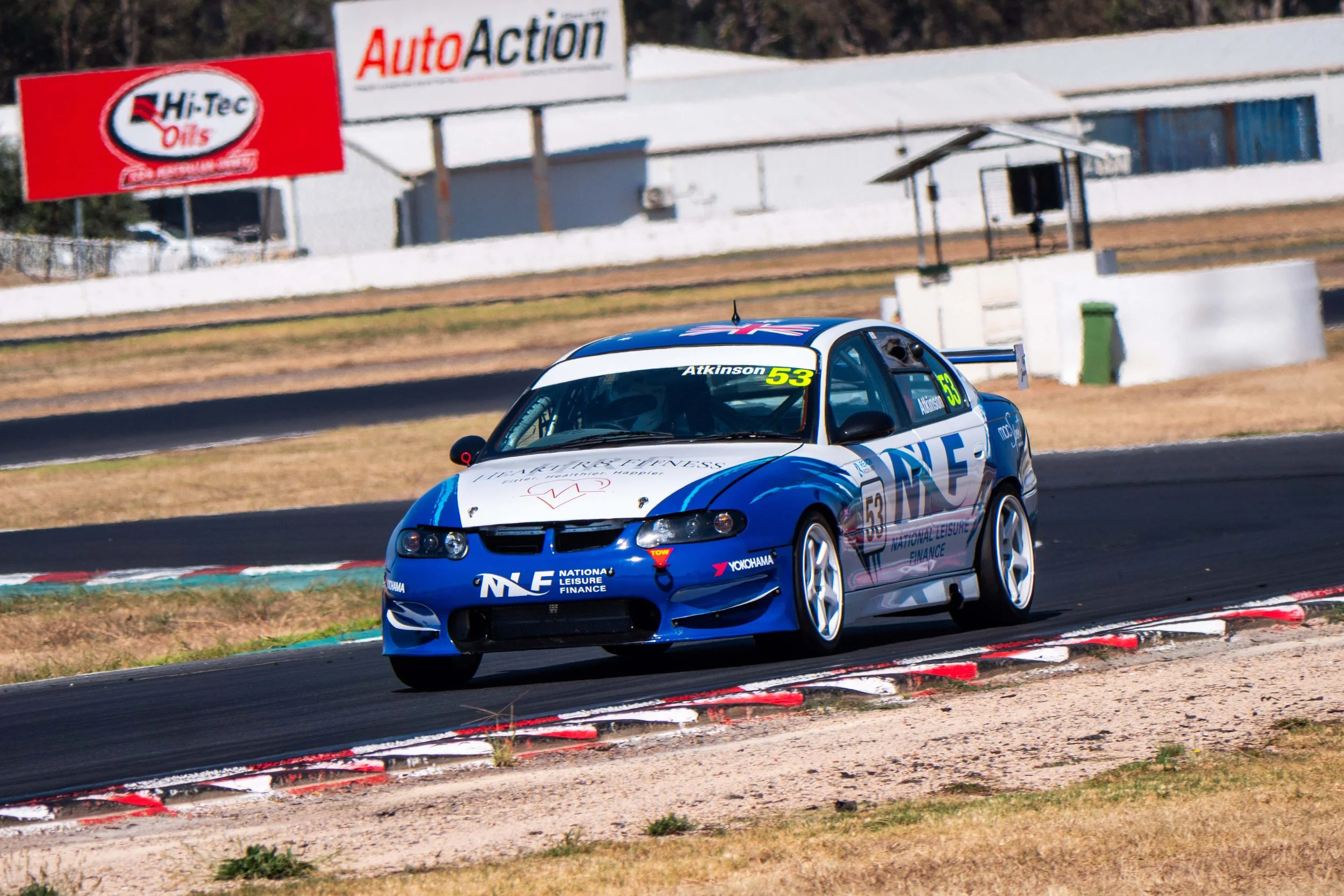 Blue race car with the number 53 navigating a turn on a racetrack.