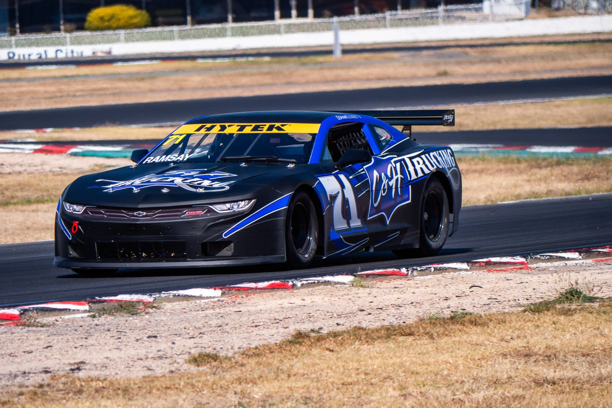 Race car on a track, black with blue accents, sponsored by C & D Trucking, with the number 7, and a yellow banner with HYTEK on top.